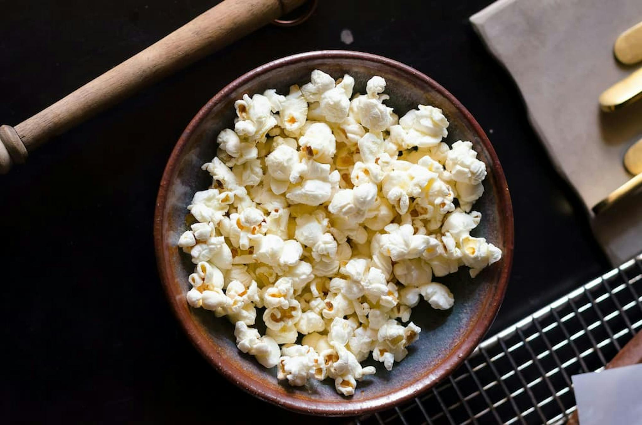 A bowl of freshly popped popcorn sits on a dark surface. The popcorn is light and fluffy, filling the bowl to the brim.