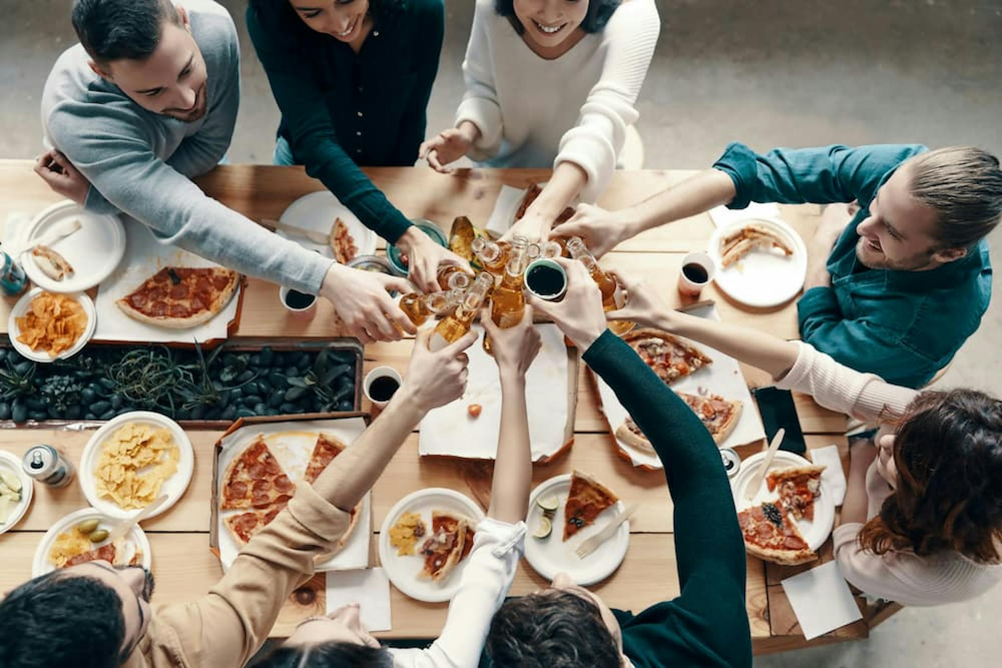 A group of friends toasting while sharing a meal with pizzas and snacks