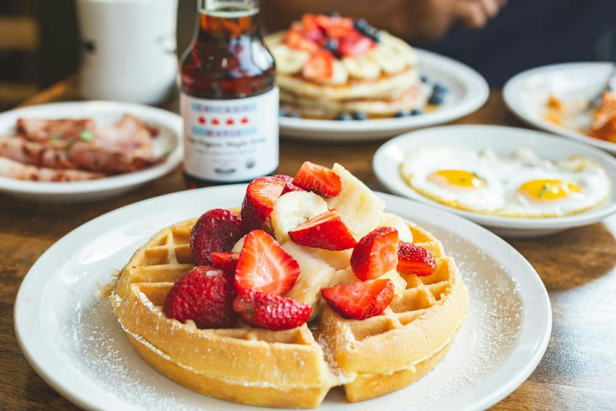 Delicious waffles with fresh strawberries and banana slices, accompanied by coffee and other dishes on a breakfast table.