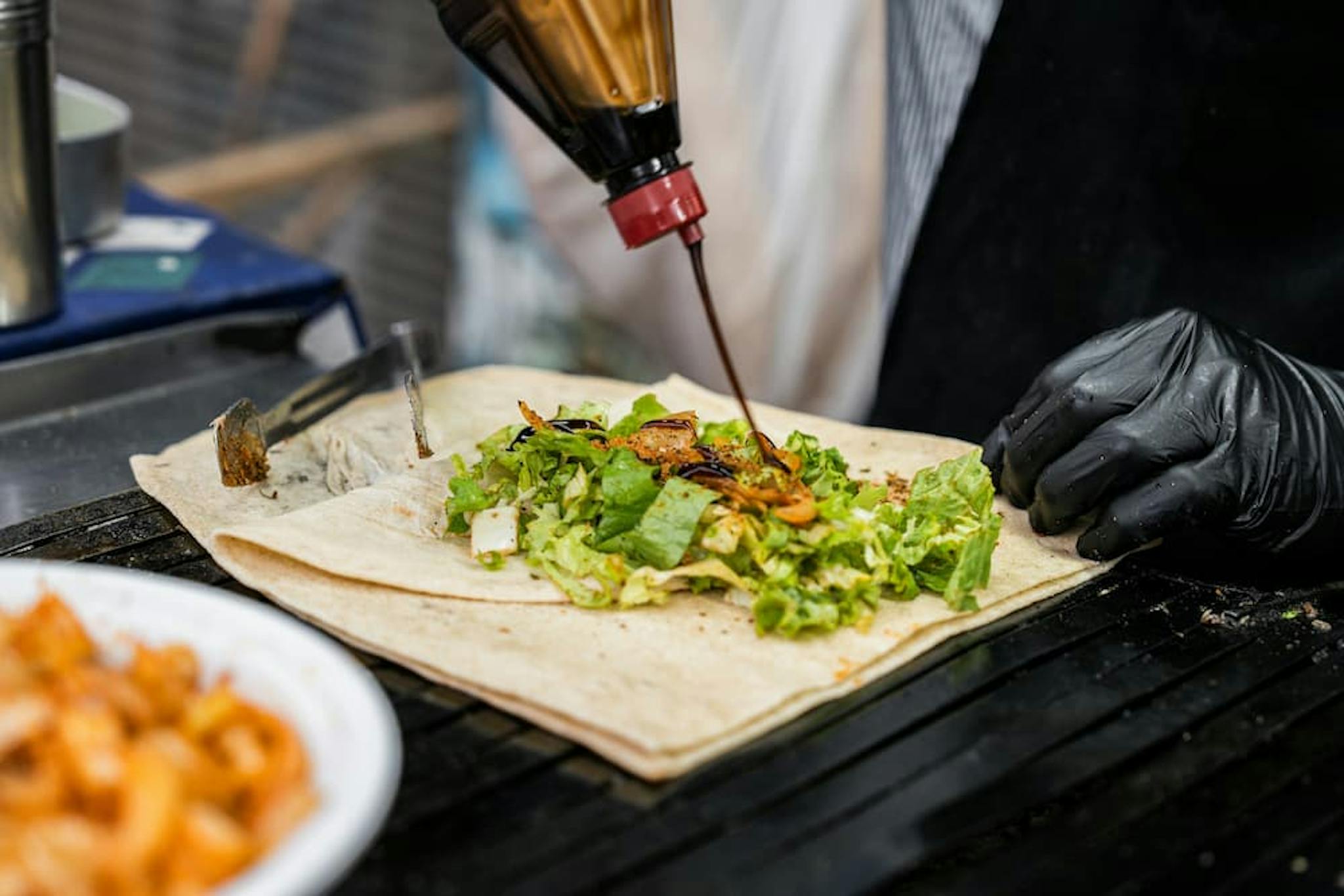 A chef adding sauce to a wrap filled with lettuce and other ingredients.