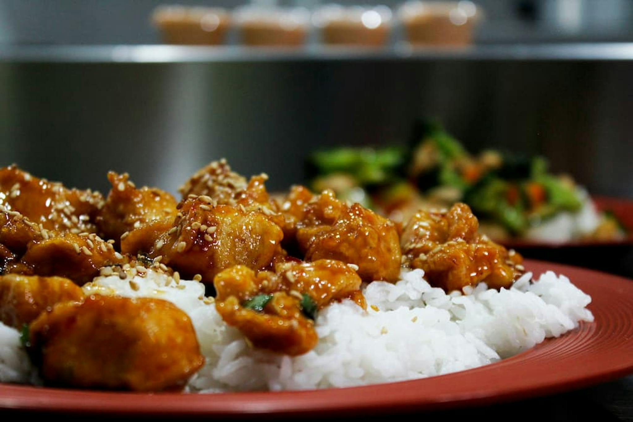 Colorful plate with sweet and sour chicken accompanied by white rice and sesame seeds.