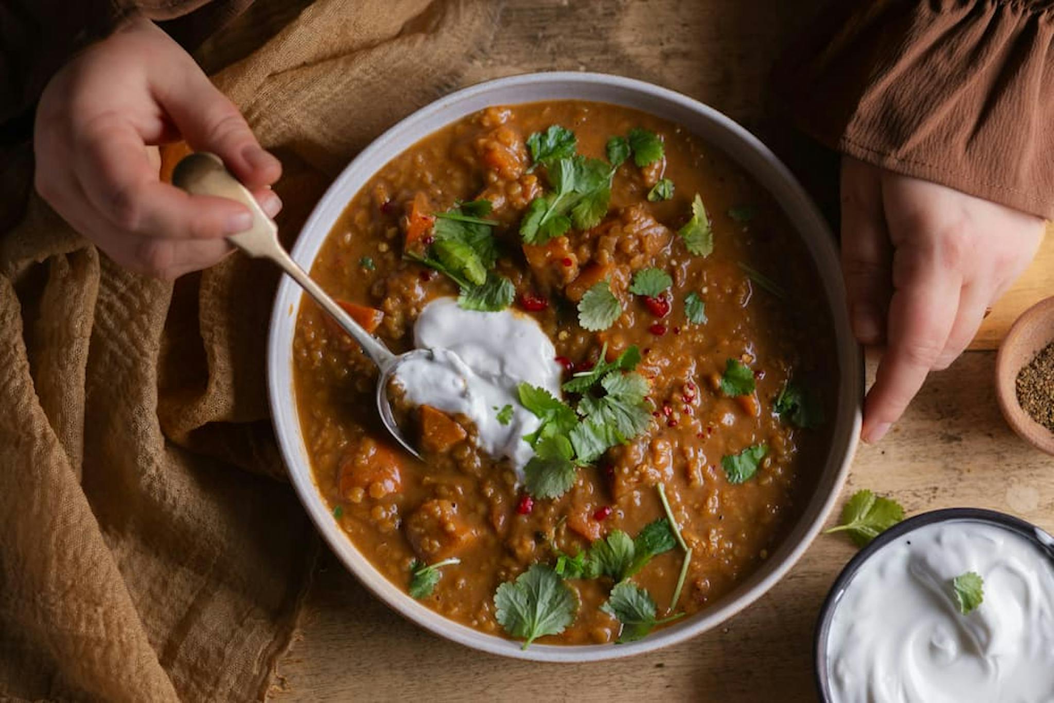 A bowl of curry with a spoon serving the meal, garnished with fresh cilantro and a touch of yogurt