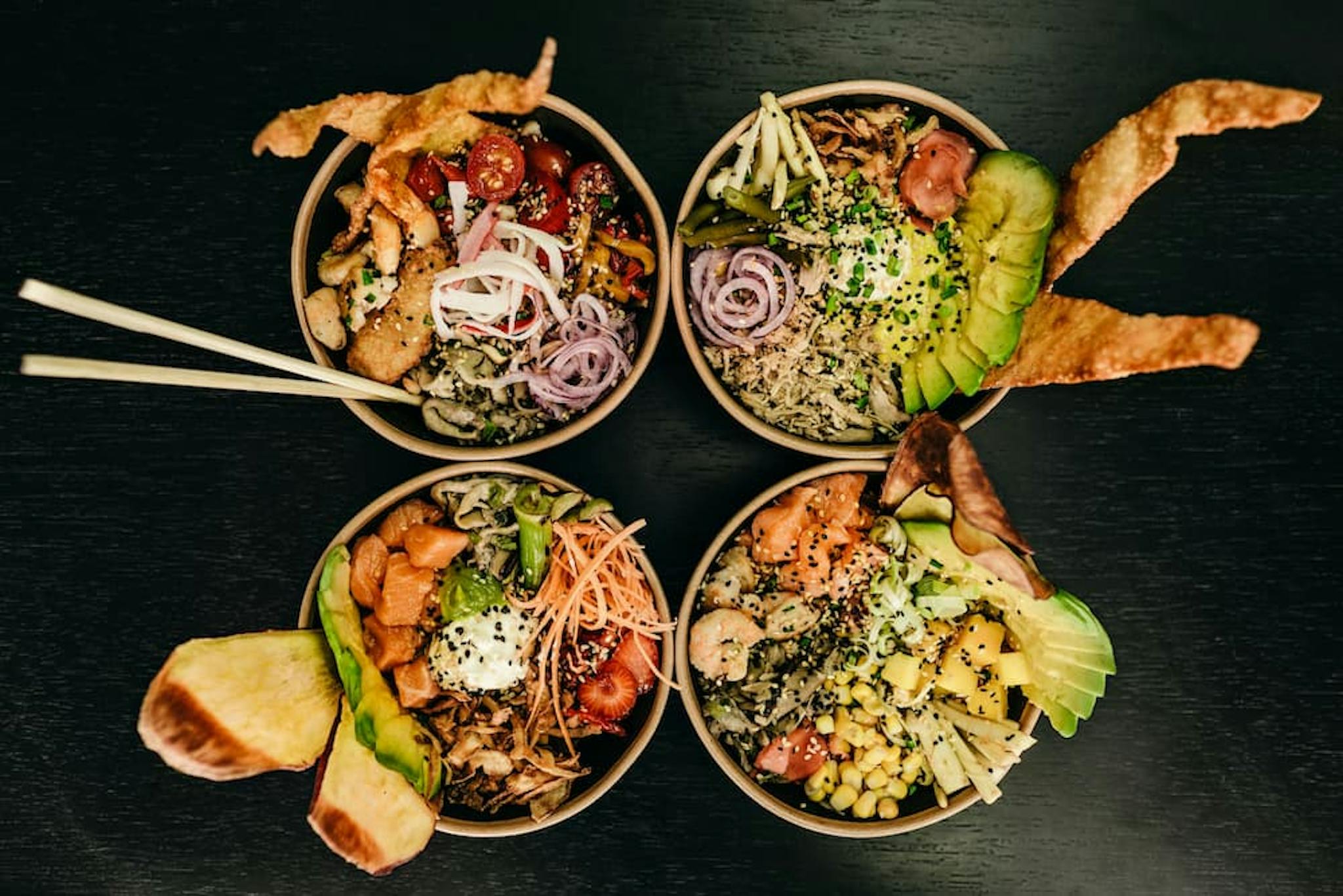 Assorted poke bowls presented in bowls with fresh ingredients like avocado, salmon, and colorful vegetables, served with chopsticks.