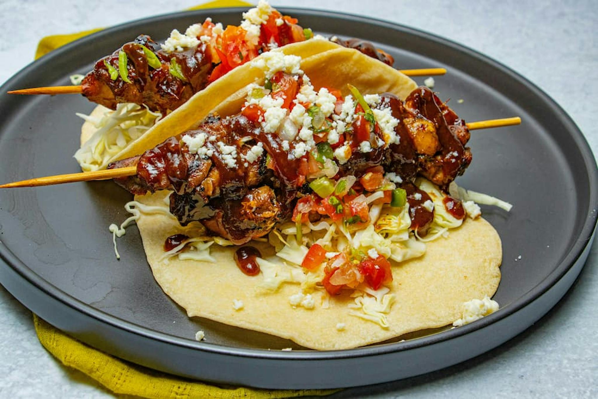 Meat skewers on tortillas, accompanied by tomatoes, onions, and cheese