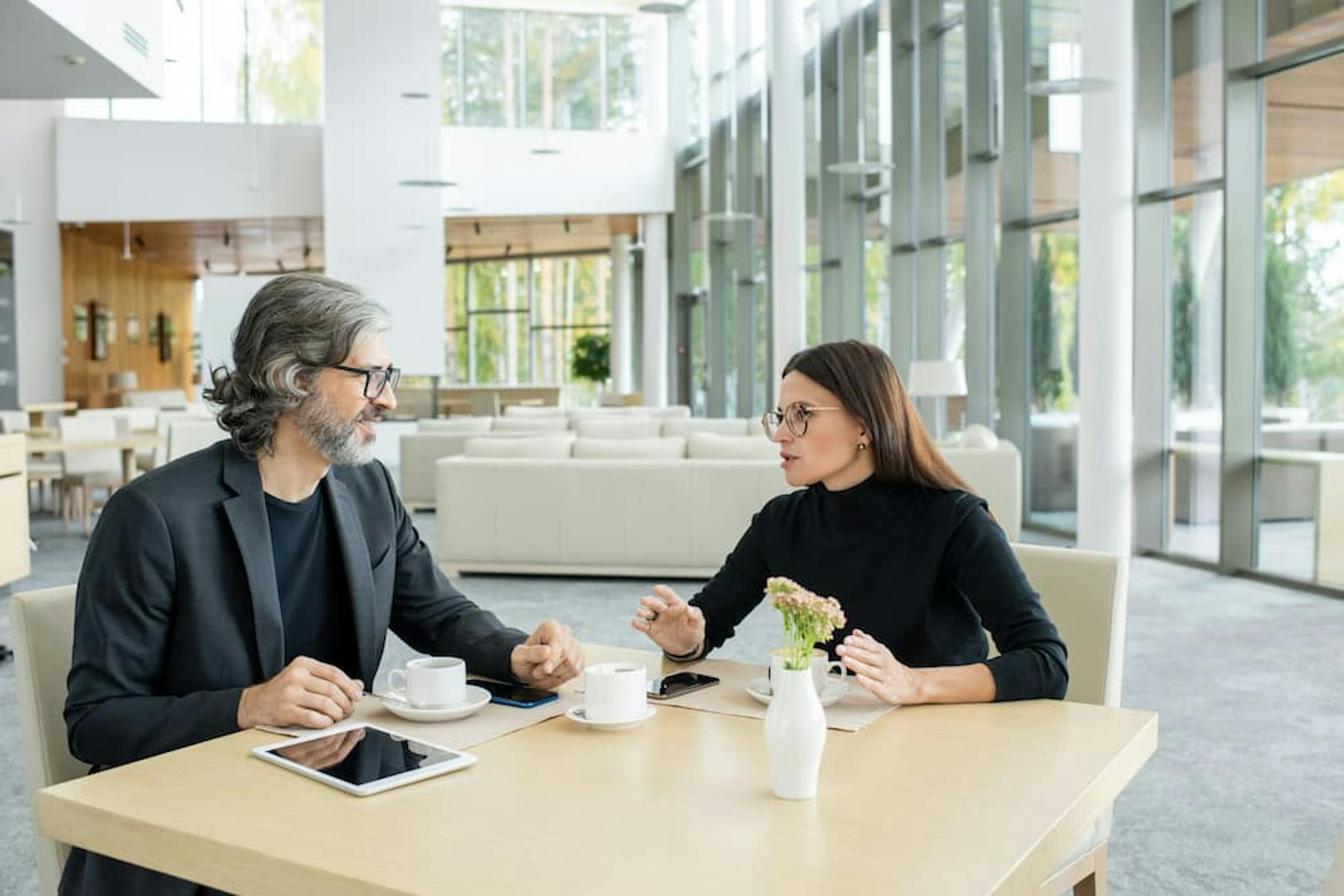 Two professionals discussing ideas in a modern and cozy environment, with a table filled with office items and a decorative plant.