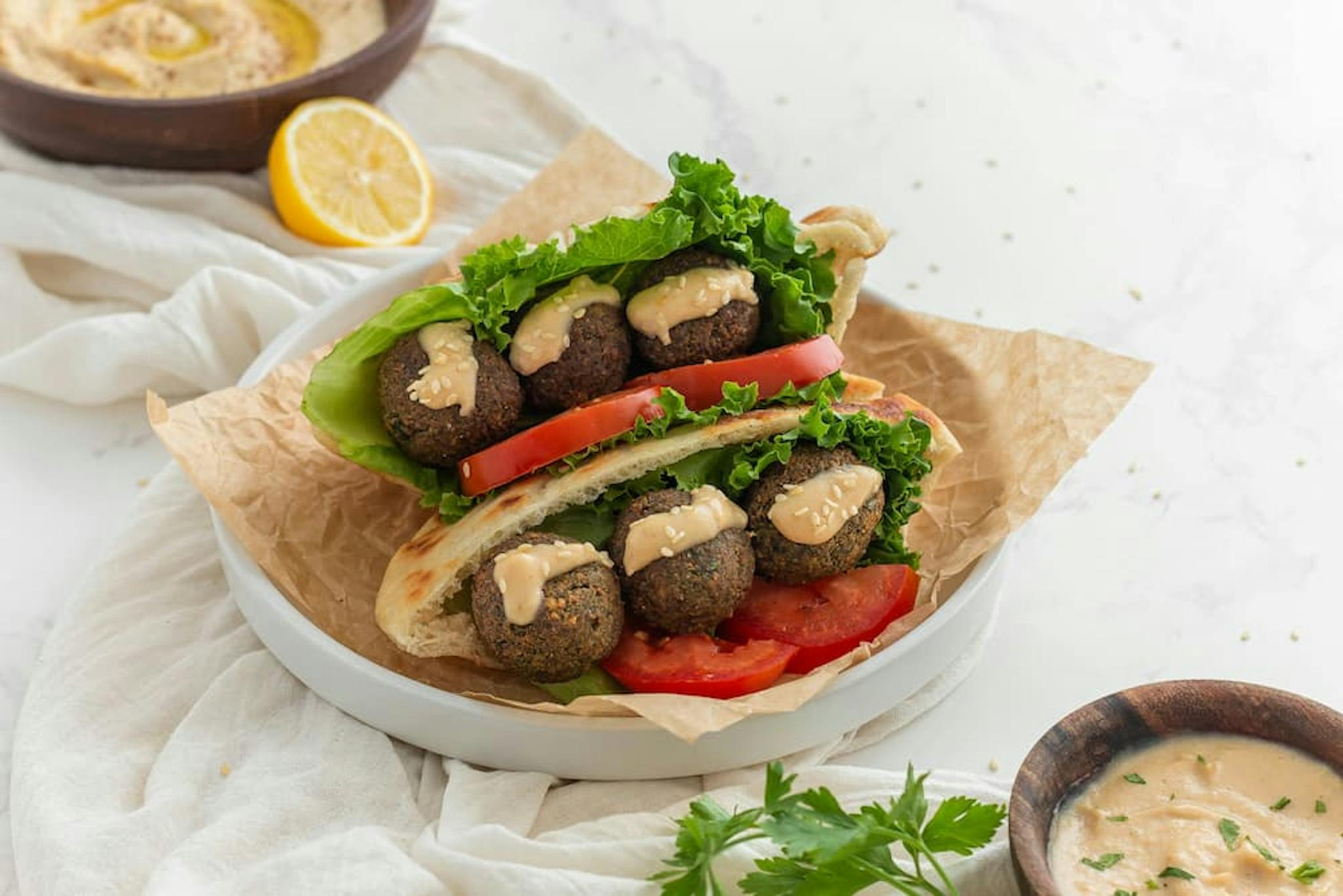 Falafels served in pita bread, accompanied by lettuce leaves, tomato, and sauce.