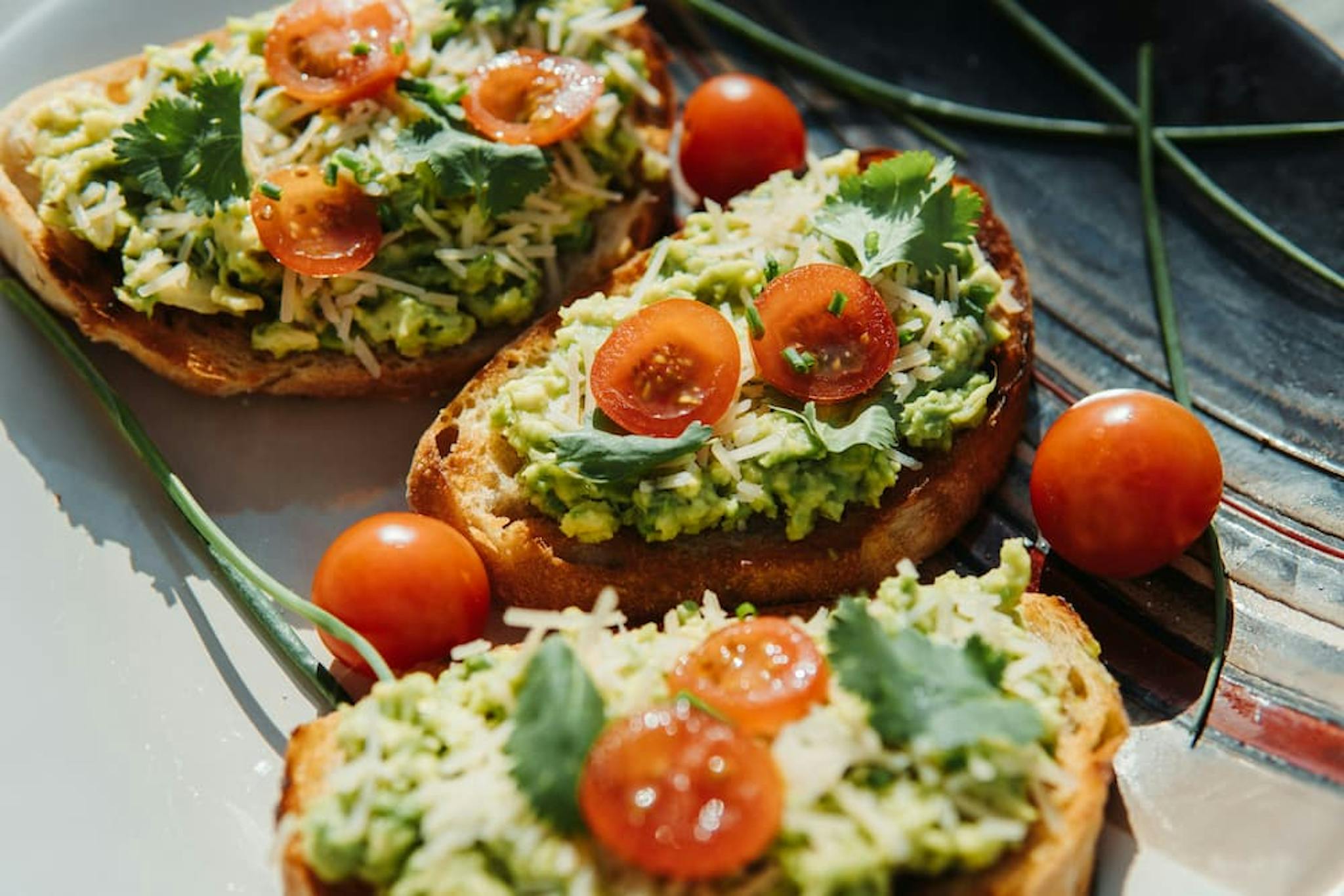 Toasts with avocado spread, grated cheese, and cherry tomatoes, garnished with fresh cilantro.