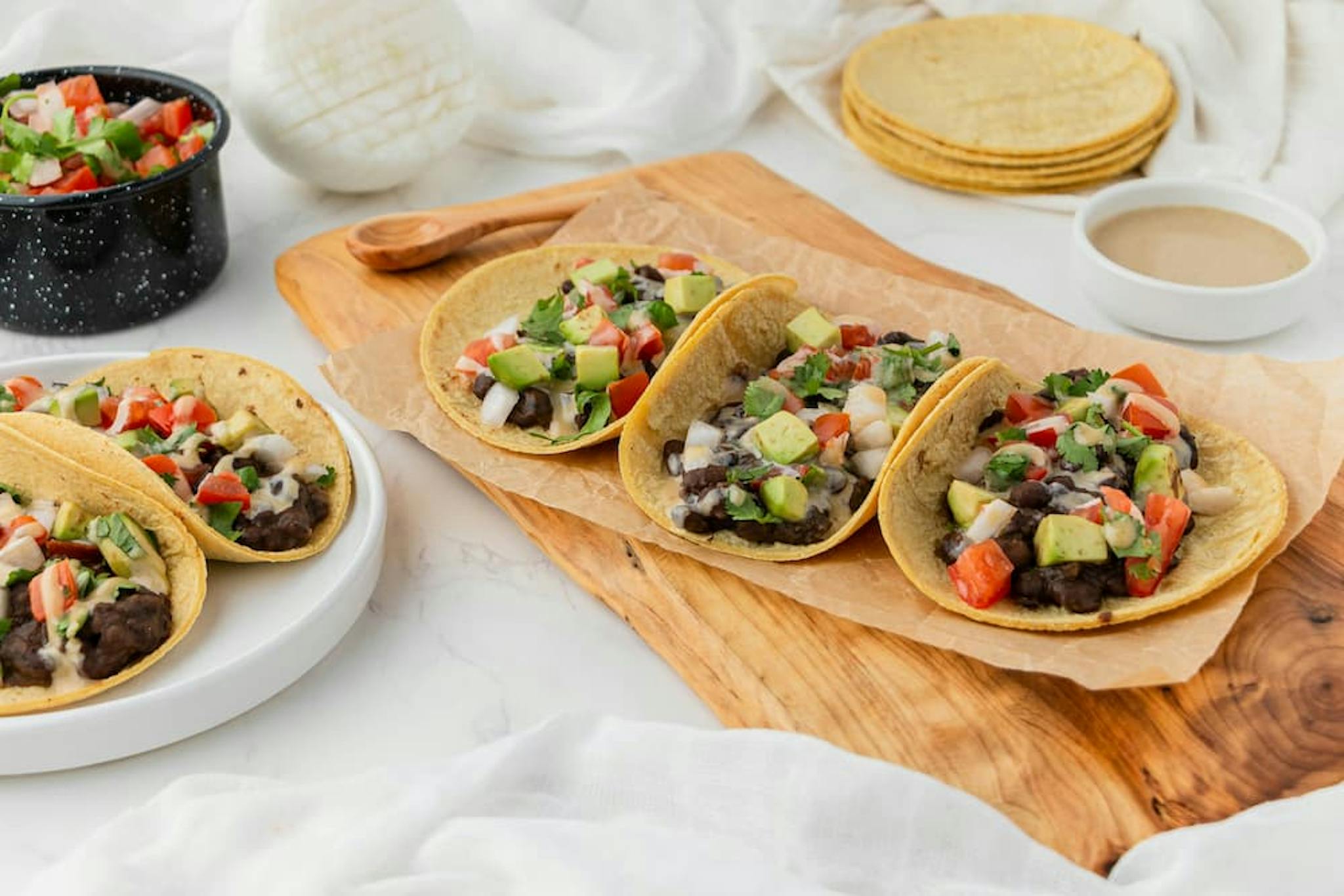 Tacos with beef, avocado, tomato, and onion, served on a plate and wooden board.