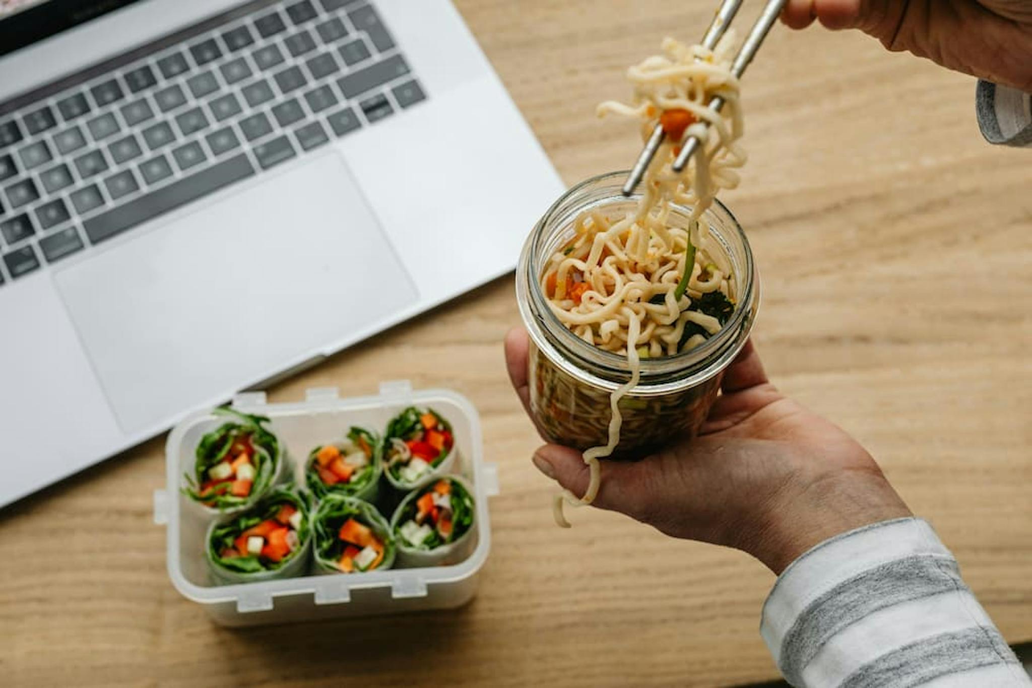 A hand holding chopsticks while pulling instant noodles from a glass bowl.