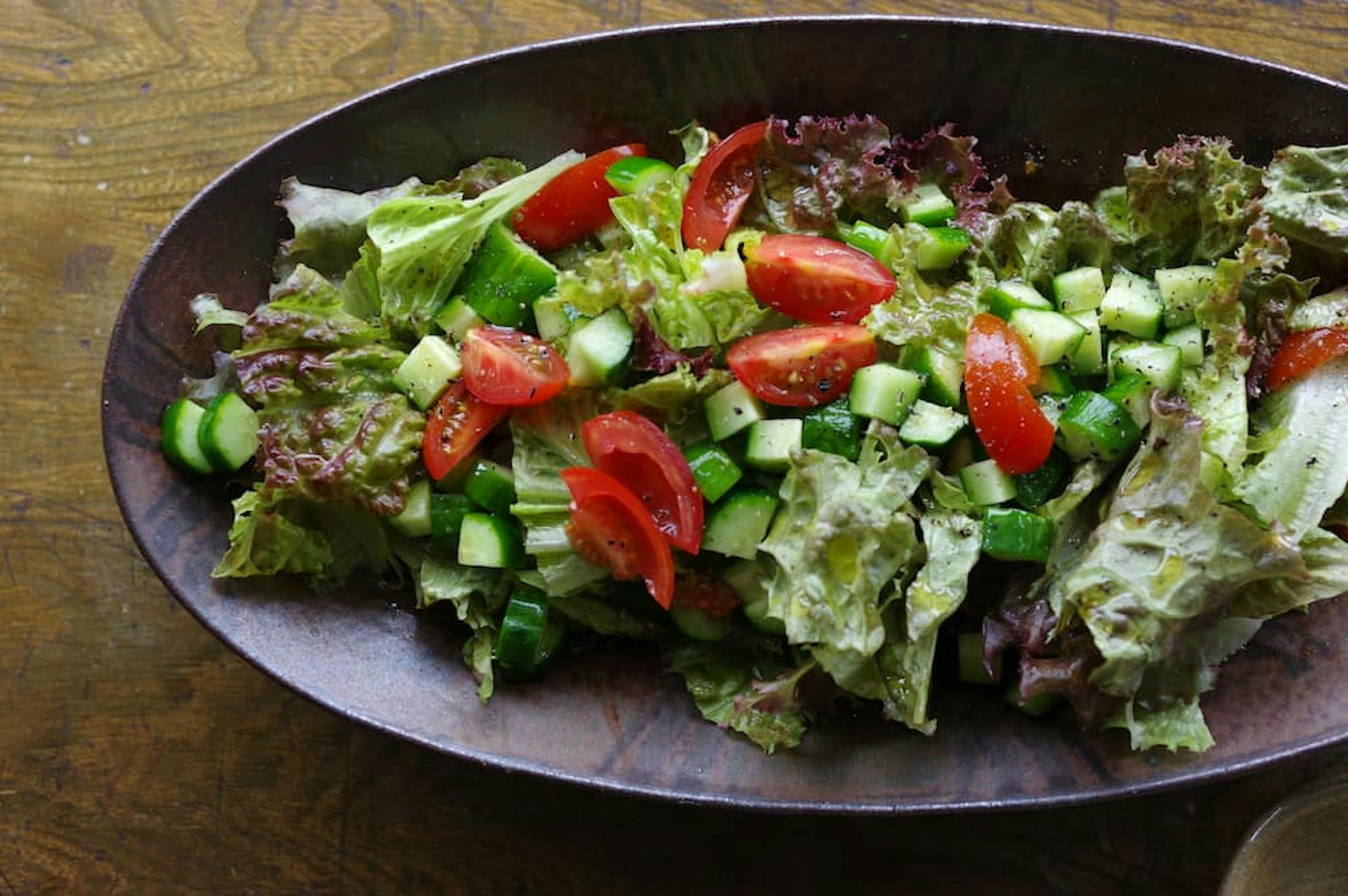 Fresh salad with lettuce, tomatoes, and cucumbers in a dark bowl.