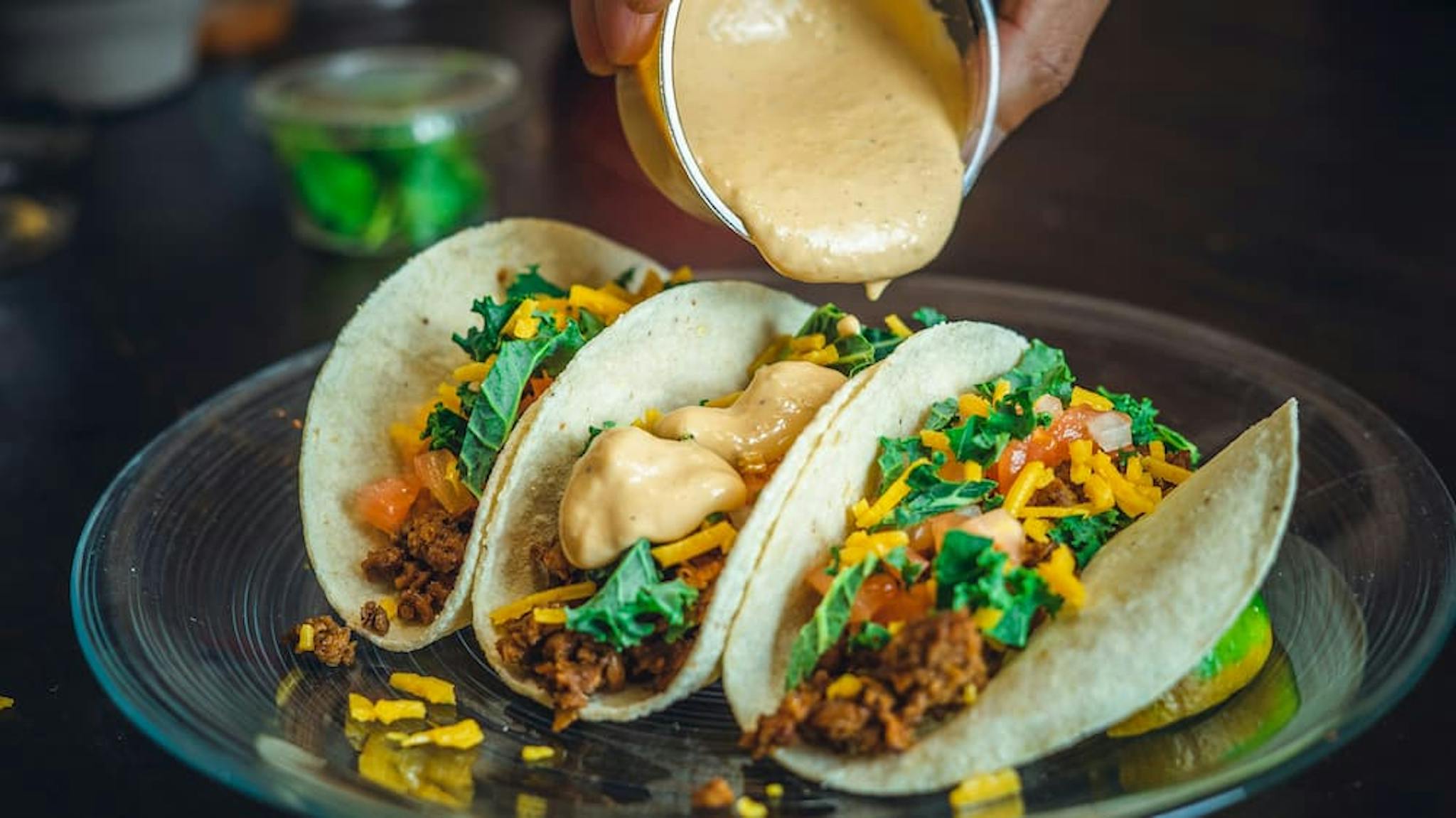 Delicious tacos filled with ground beef, cheddar cheese, fresh tomato, and creamy sauce being served on a plate.