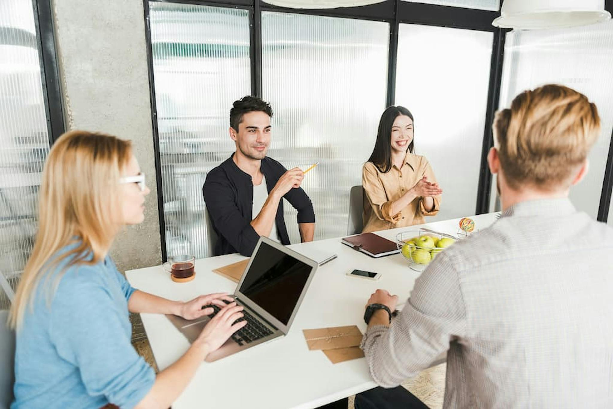 A group of four colleagues is seated around a white table in a modern office setting, engaged in a discussion.