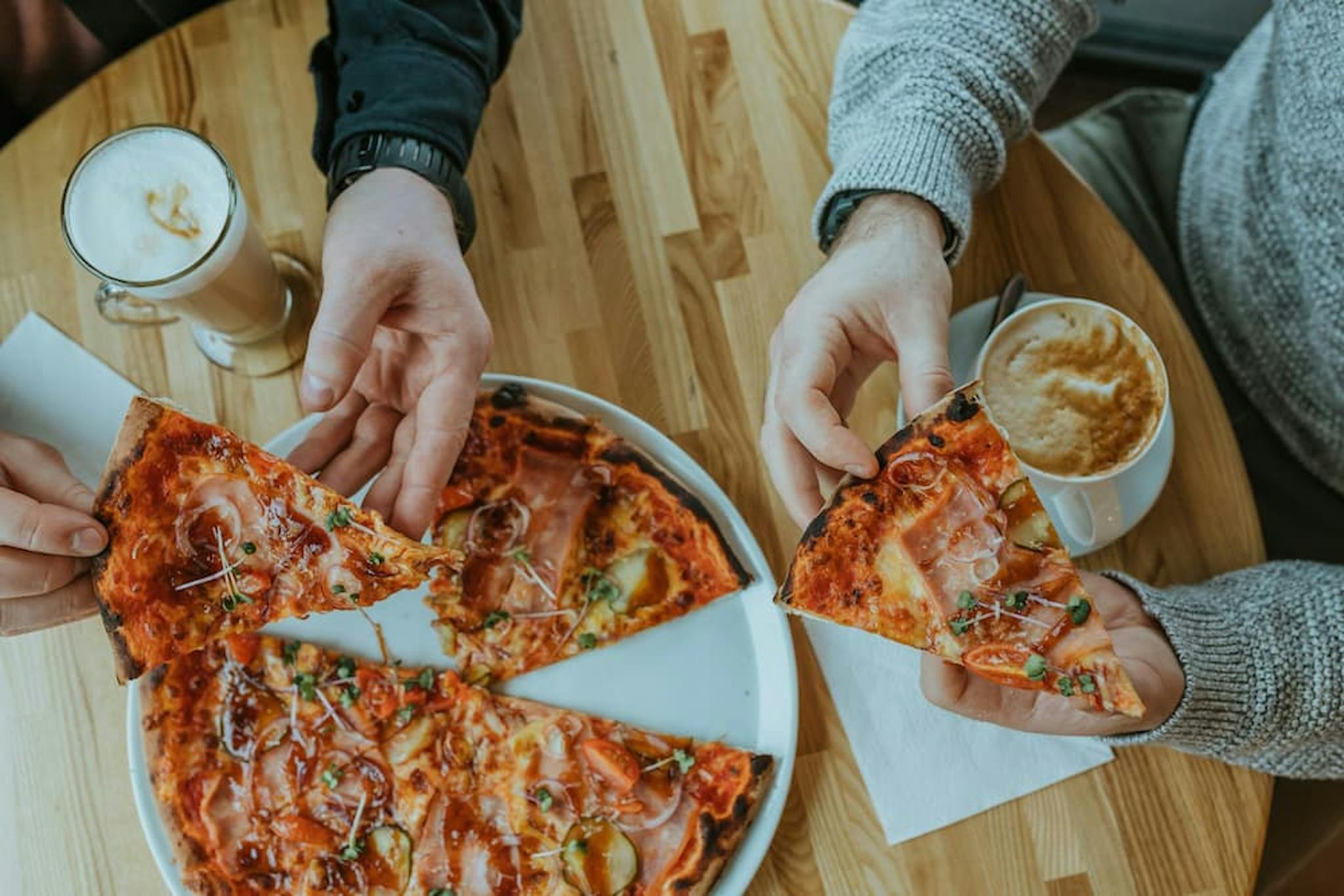 Two people are sitting at a wooden table, each holding a slice of pizza.