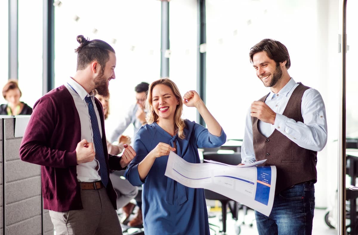A group of people collaborates in a modern office setting. One person holds a large sheet of paper with diagrams, while others participate actively in the discussion.