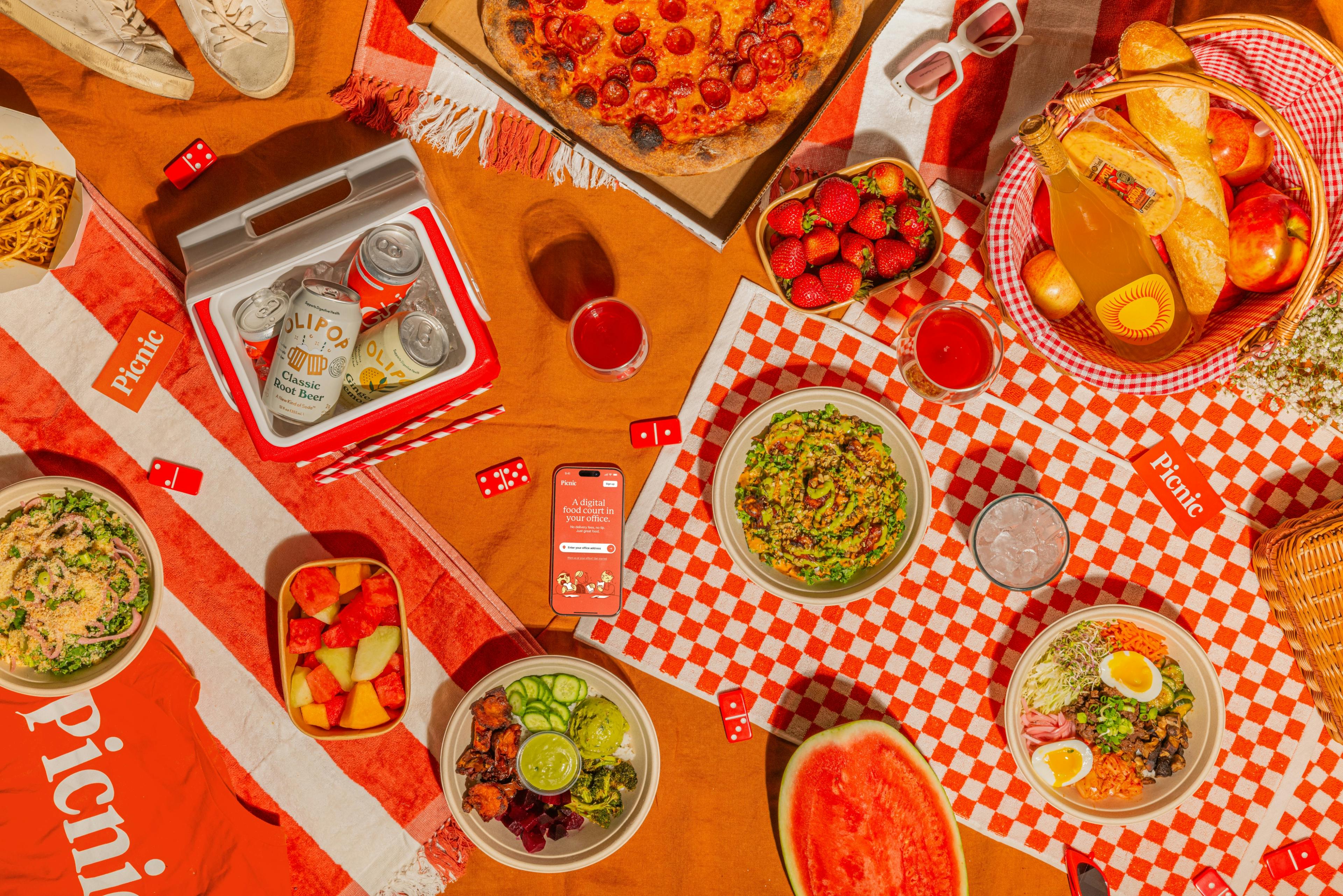 An overhead shot of a picnic with Olipops, pizza, strawberries, watermelon, and other foods.