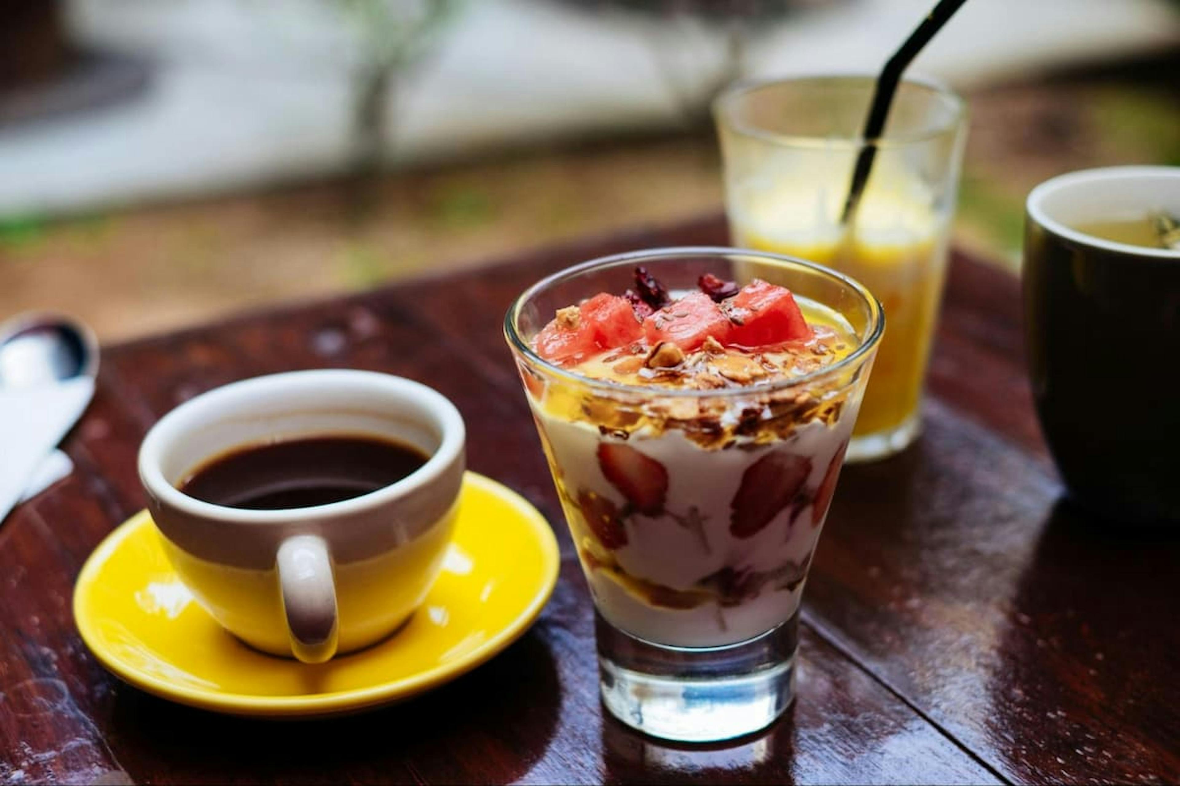 Image of a cup of coffee next to a glass of fruit salad.