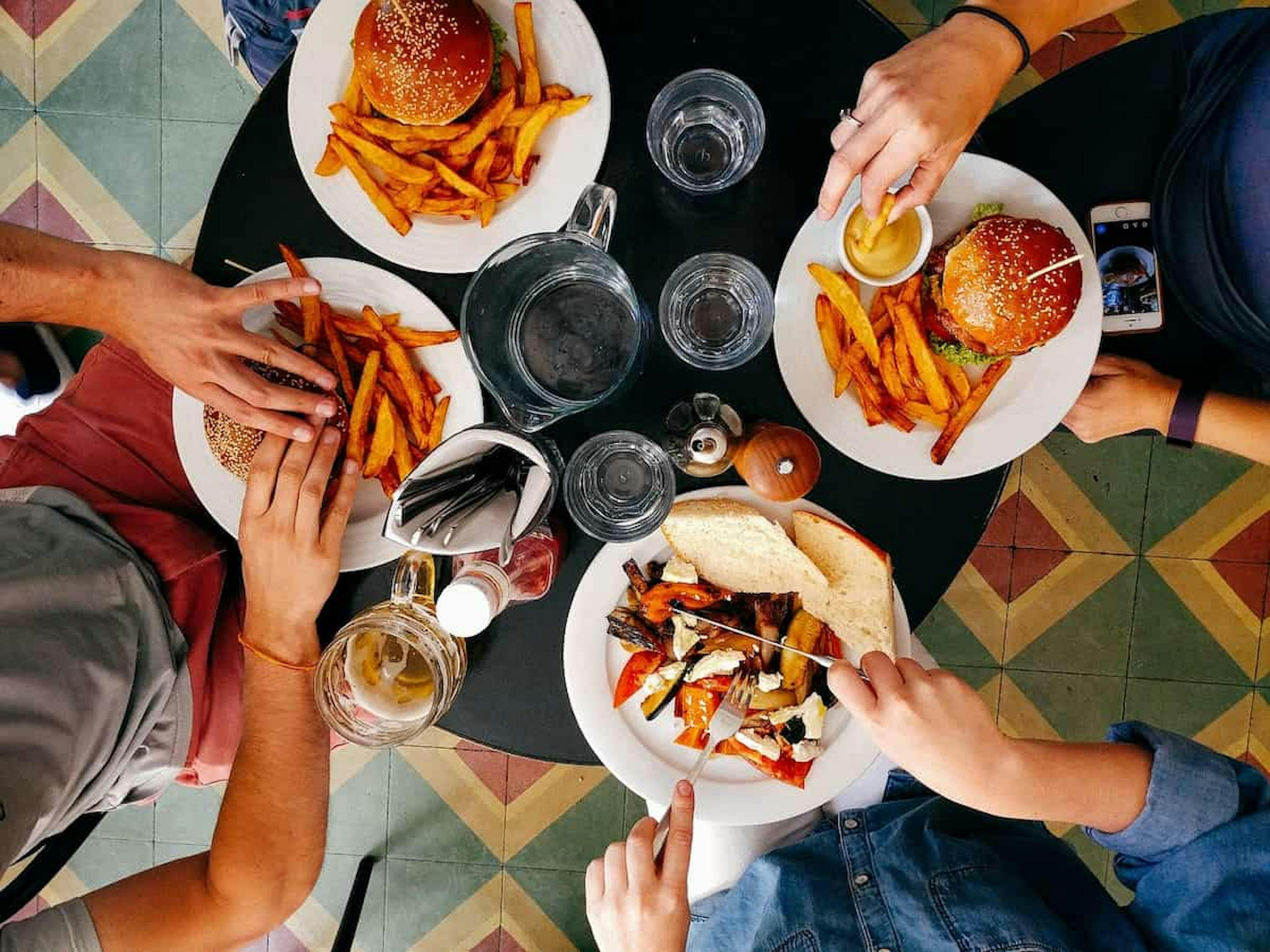 Top view of a table with friends enjoying burgers, fries, and roasted vegetable sandwiches, creating a casual dining experience.