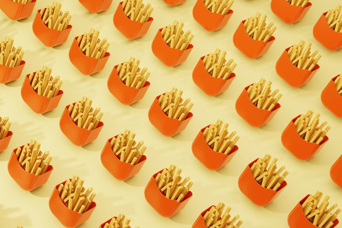 Multiple servings of French fries in bright orange containers arranged in a geometric pattern on a light yellow background.