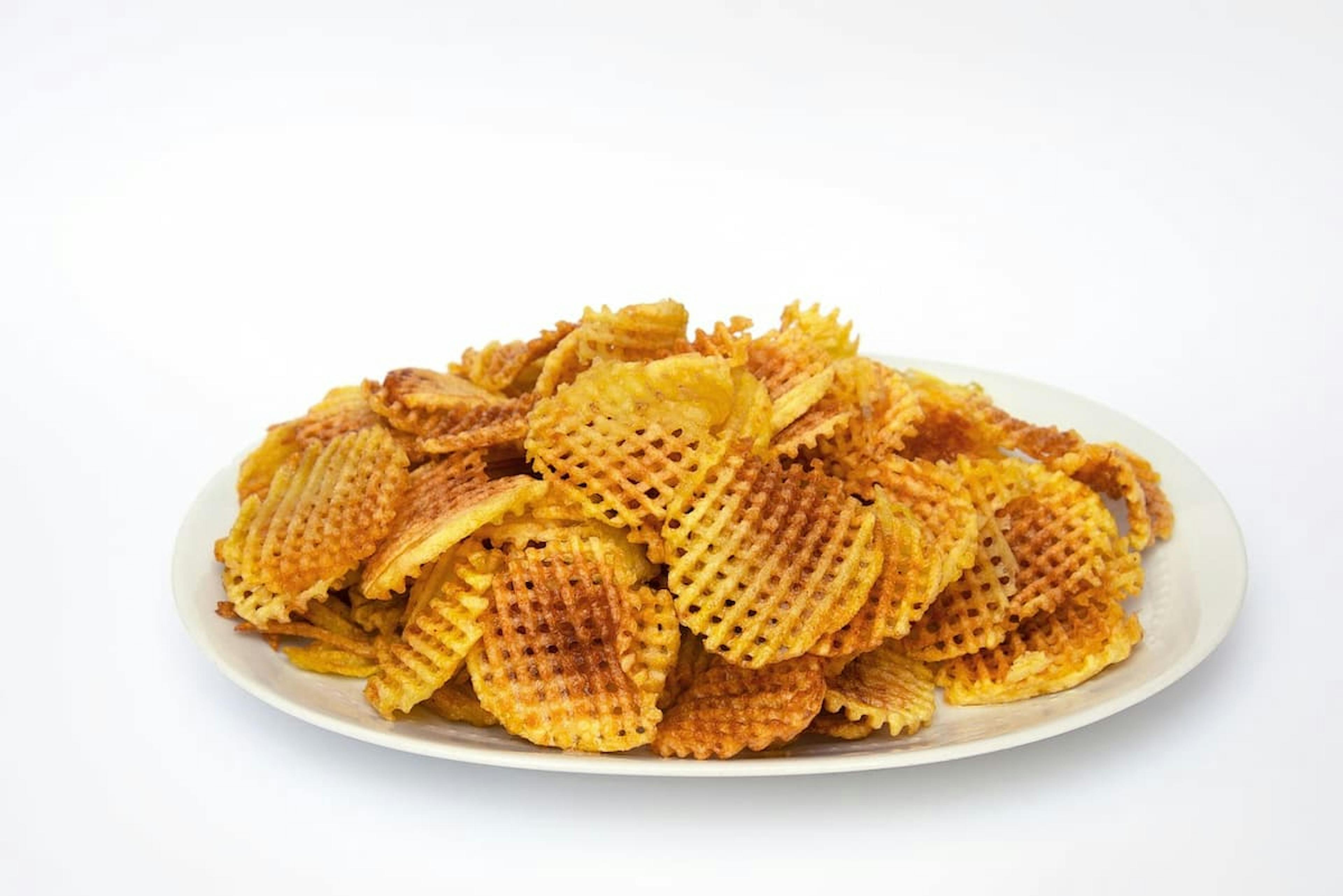 Plate of crispy waffle-cut potato chips stacked high, with a golden-brown texture against a plain white background.