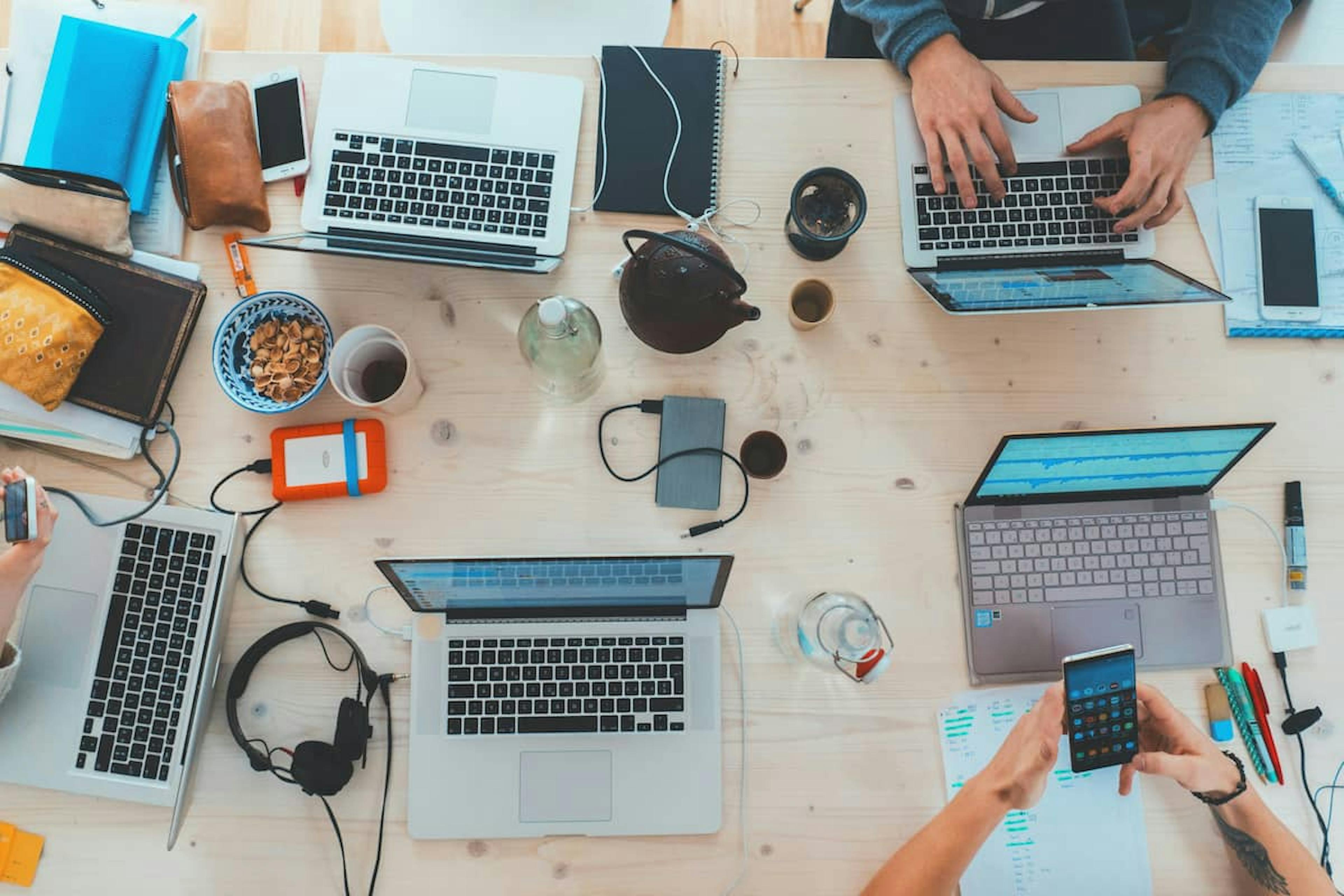 Top view of a workspace with several laptops, accessories, and a person holding a smartphone.