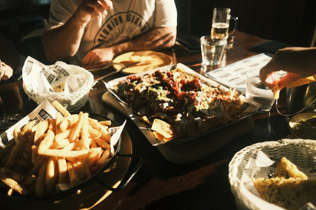 A table is set with a generous spread of food, including a large plate of loaded nachos, a basket overflowing with french fries, and another basket with what appears to be fried food. Two people are partially visible seated at the table, suggesting a Father's Day lunch.
