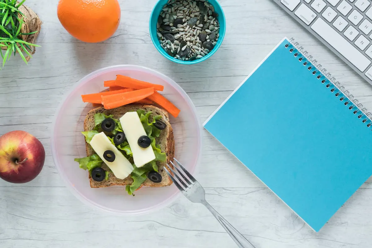 Healthy desk lunch with salad sandwich, fruits, and seeds—how to provide vegan and vegetarian lunch options in the office.