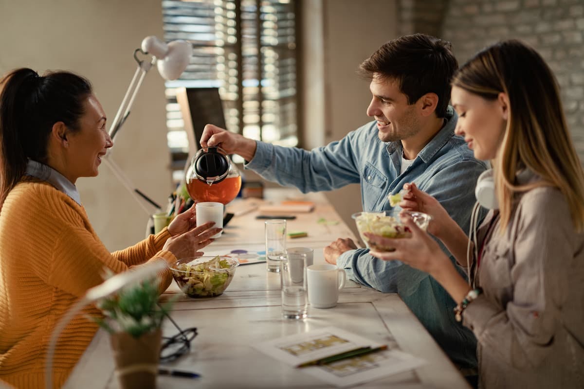 Group of coworkers enjoying a healthy meal at the office, illustrating employee lunch programs vs. traditional food allowances.