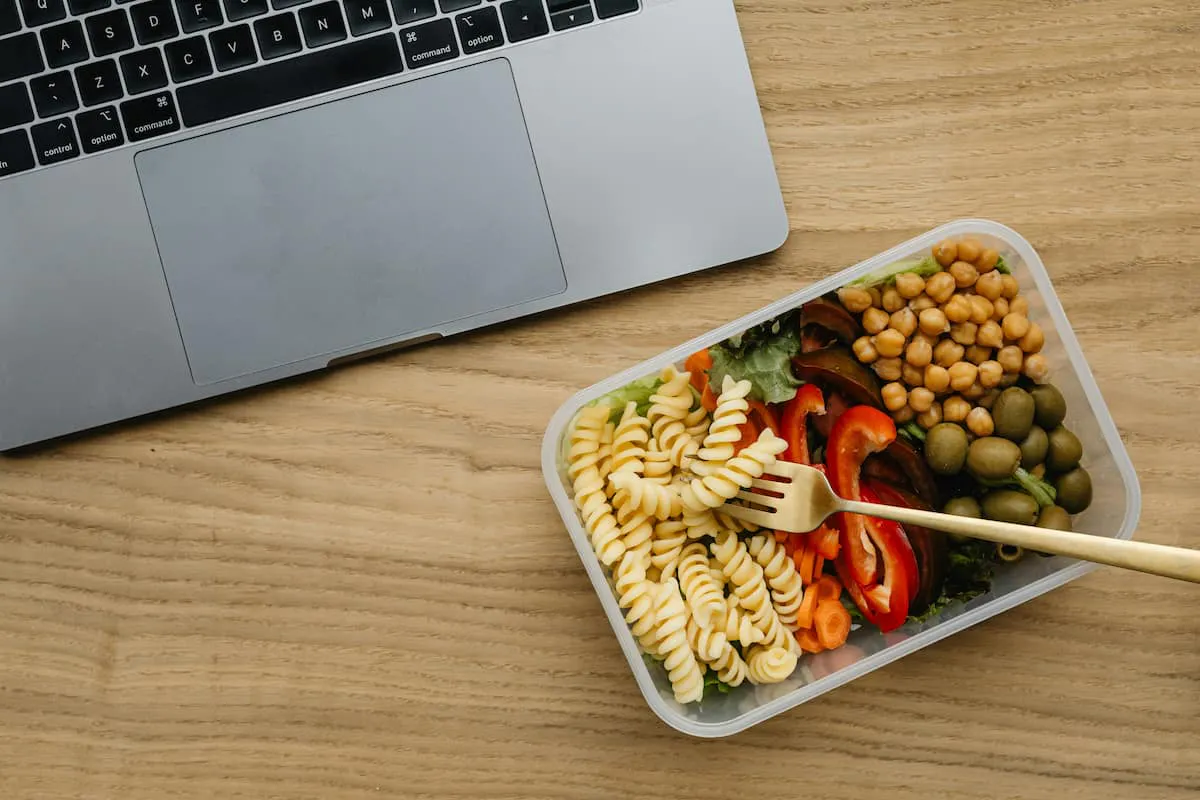Healthy lunch box with pasta, chickpeas, and veggies on desk — how to provide vegan and vegetarian lunch options in the office.