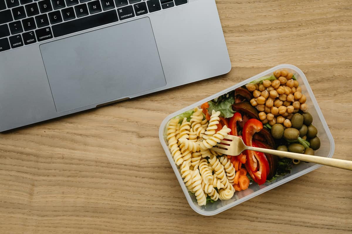 Healthy lunch box with pasta, chickpeas, and veggies on desk — how to provide vegan and vegetarian lunch options in the office.