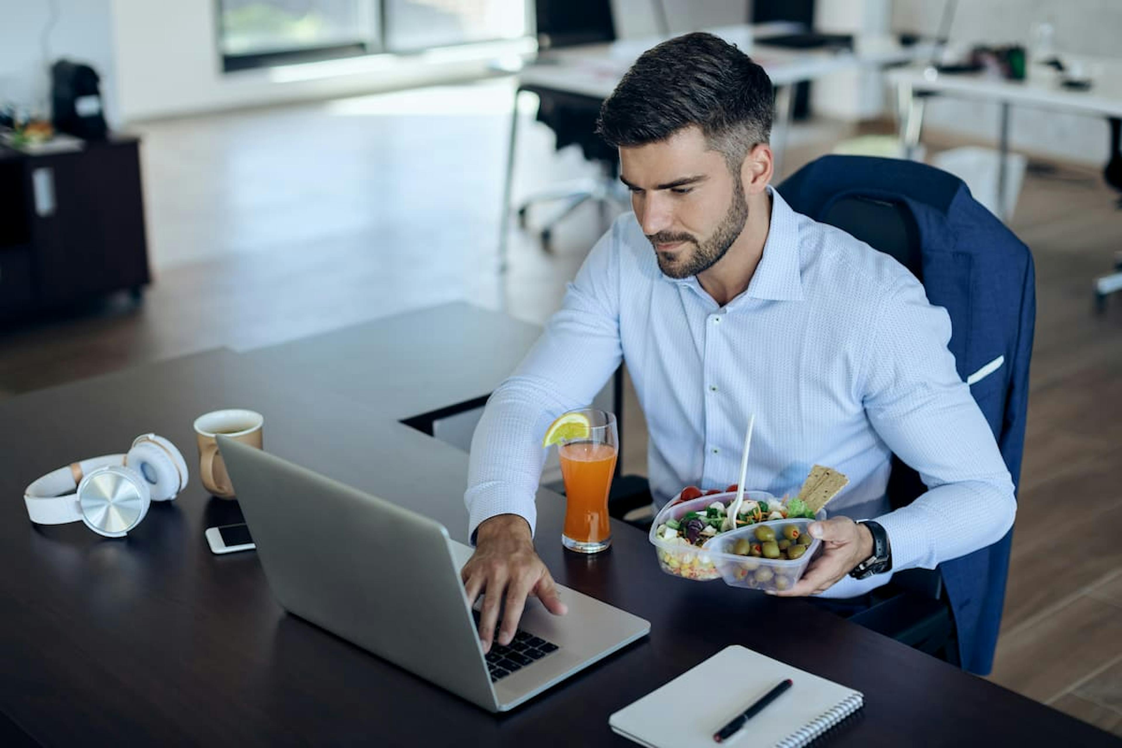 Professional eating lunch while working on laptop, highlighting the ROI of subsidized office meals for productivity.