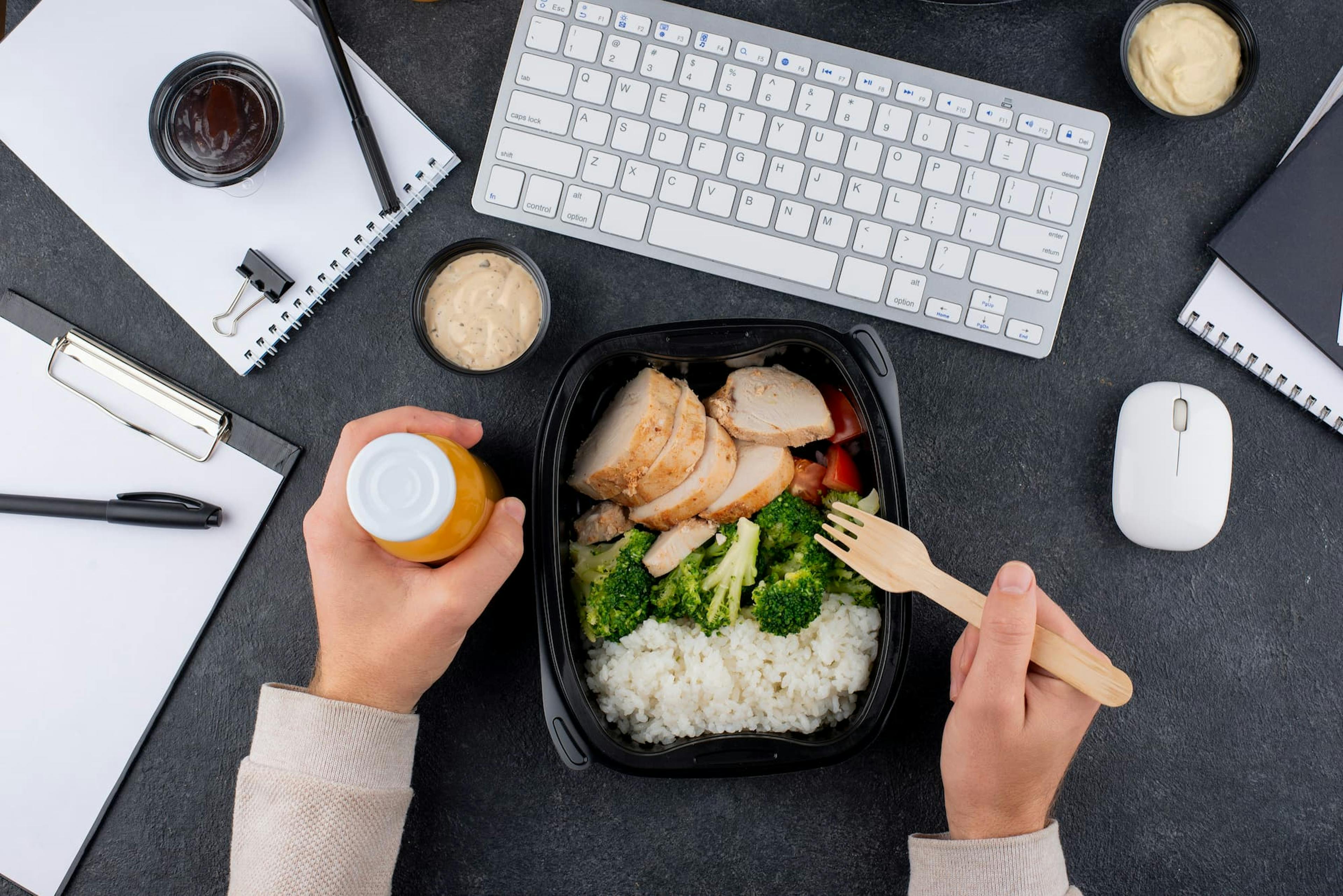 Employee eating a healthy lunch at desk, showing the ROI of subsidized office meals in a productive workspace.
