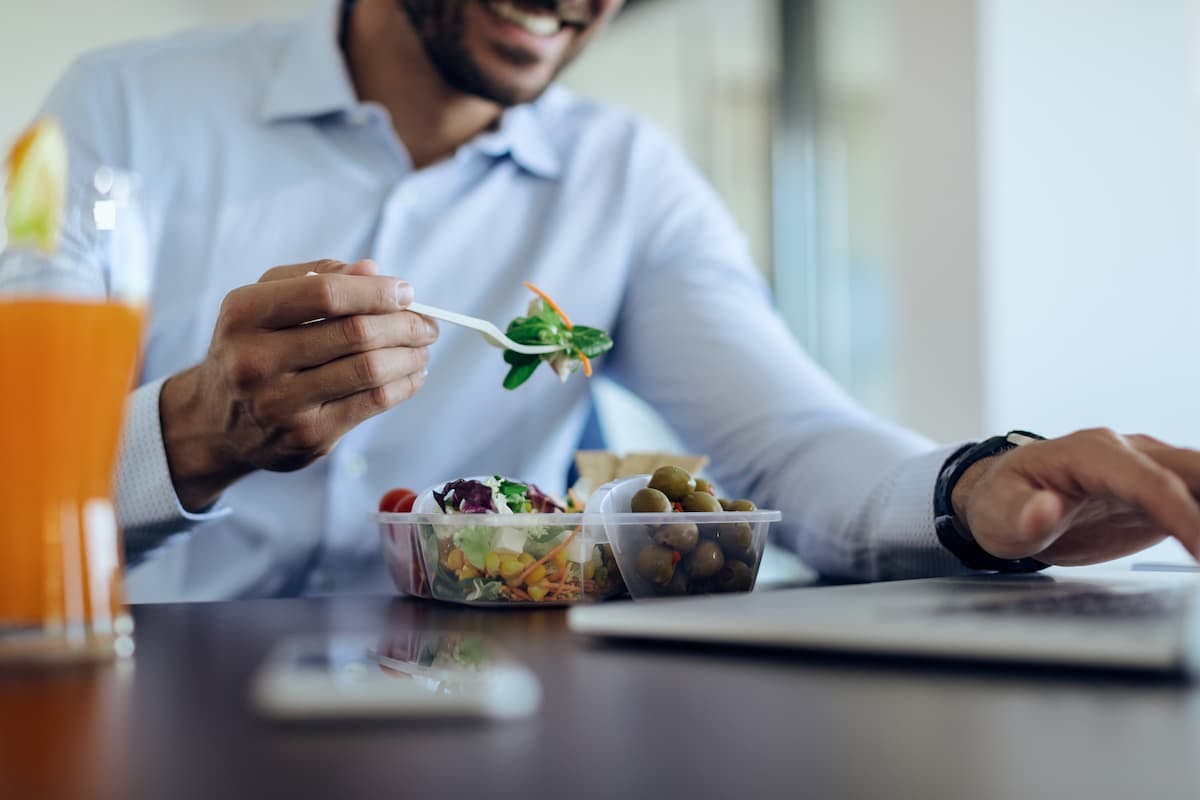 Smiling employee eating healthy lunch at desk, illustrating the ROI of subsidized office meals on morale and focus.