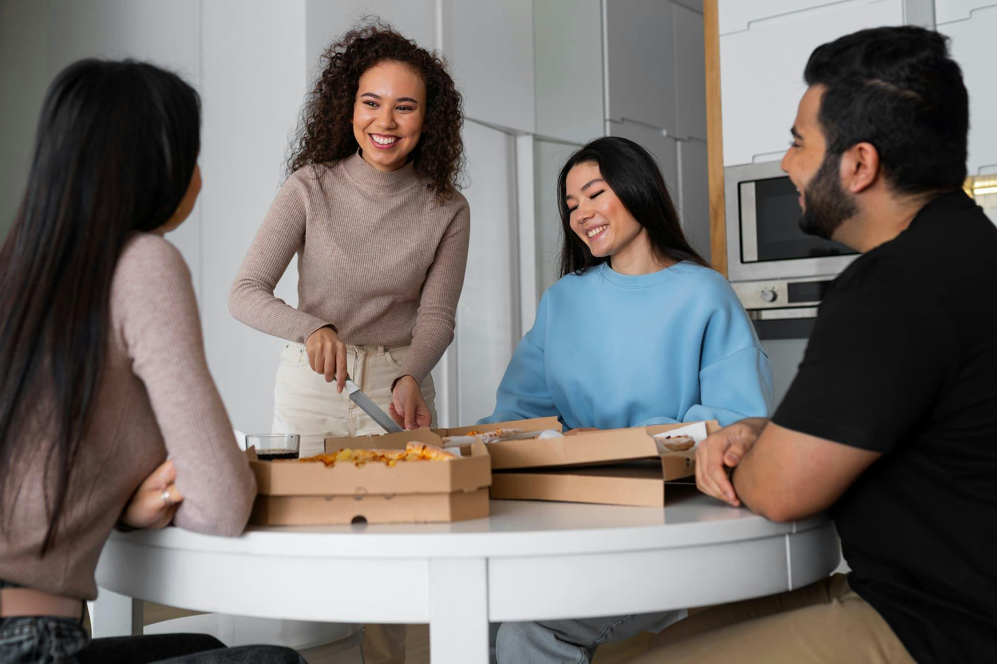 A group of colleagues enjoying pizza together at a table, discussing what to look for in an office meal delivery service.