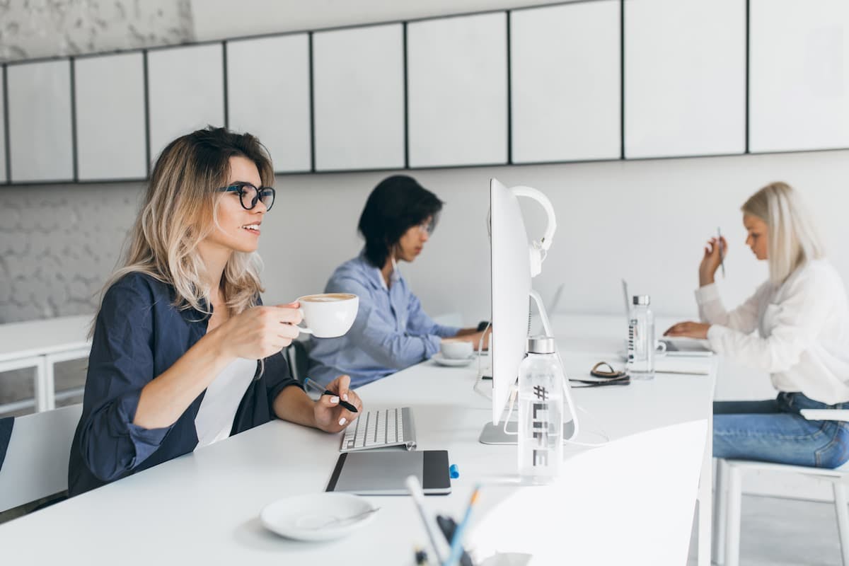 Employees enjoying coffee at their desks in a modern office, highlighting in-house cafeteria vs. meal delivery convenience.