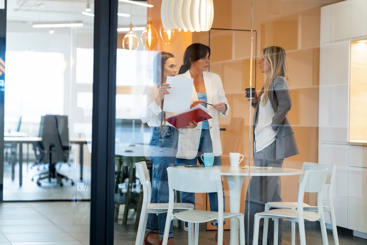 Coworkers chatting over coffee in a modern office kitchen, showing the social perks of in-house cafeteria vs. meal delivery.