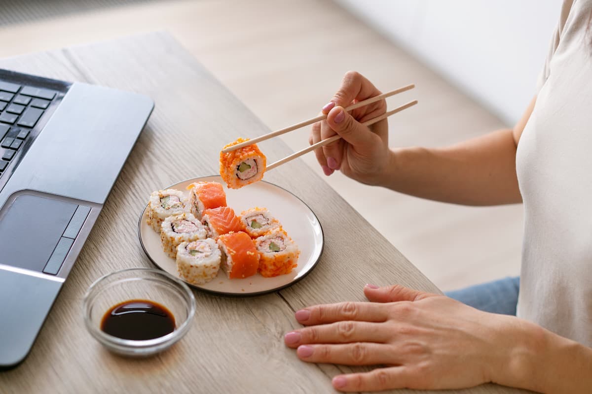 A plate of sushi beside a laptop shows one of the most popular office lunch orders enjoyed during busy workdays.