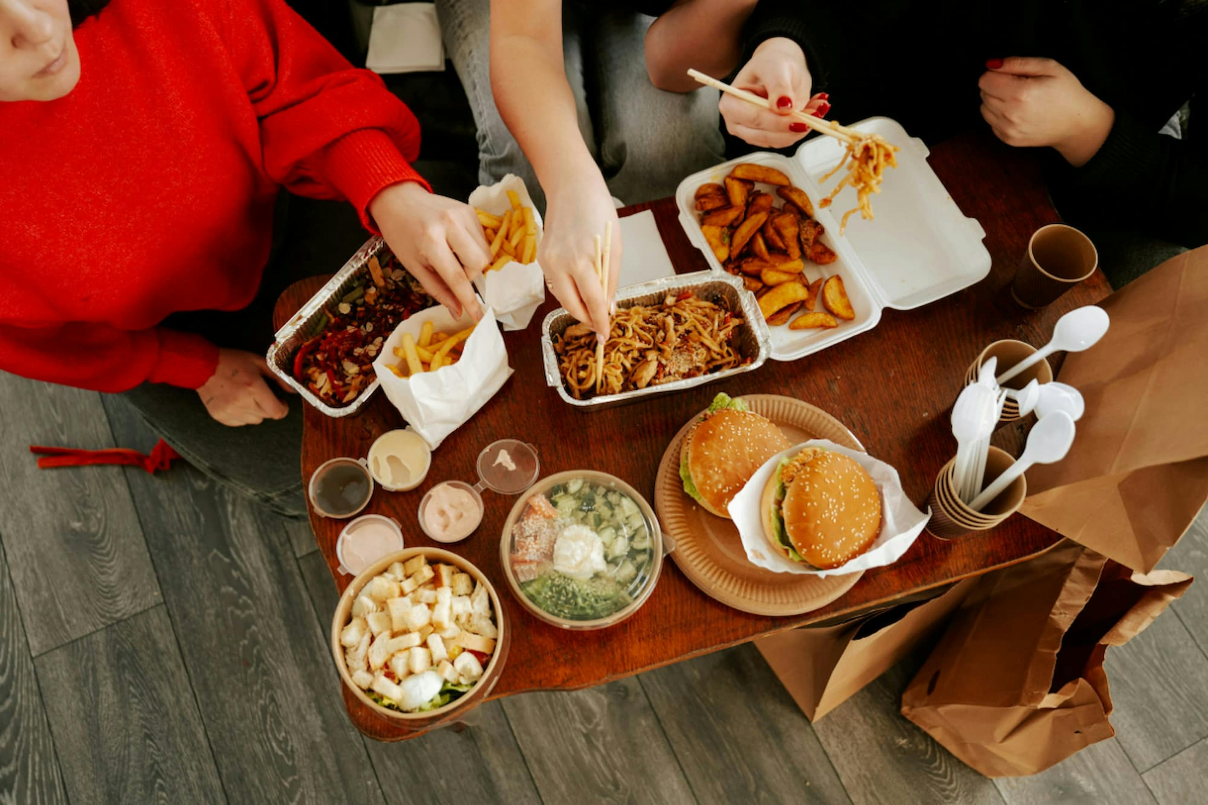 Friends sharing burgers, noodles, fries, and salad, showing the benefits of group meal ordering for variety and convenience.