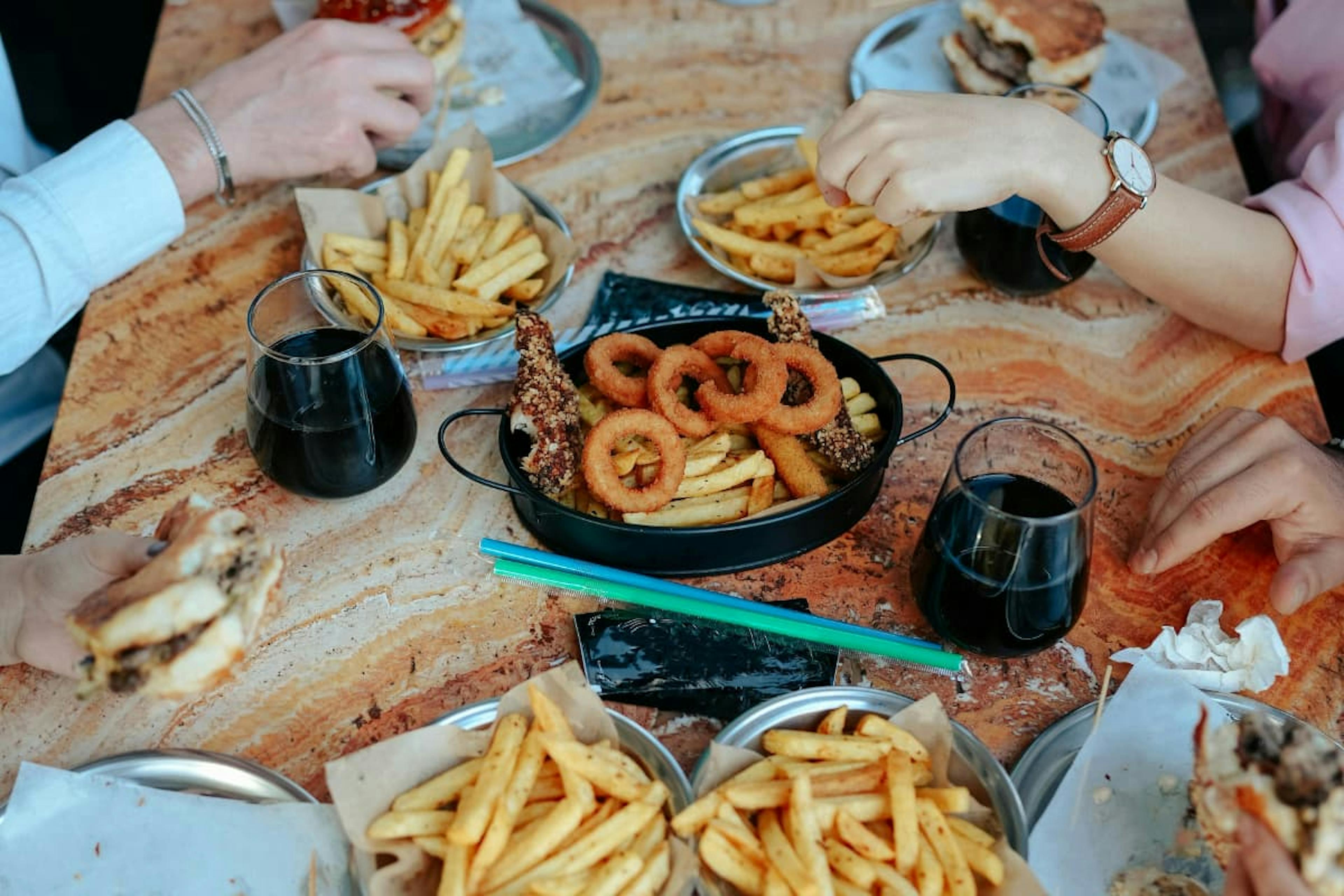Friends sharing burgers, noodles, fries, and salad, showing the benefits of group meal ordering for variety and convenience.