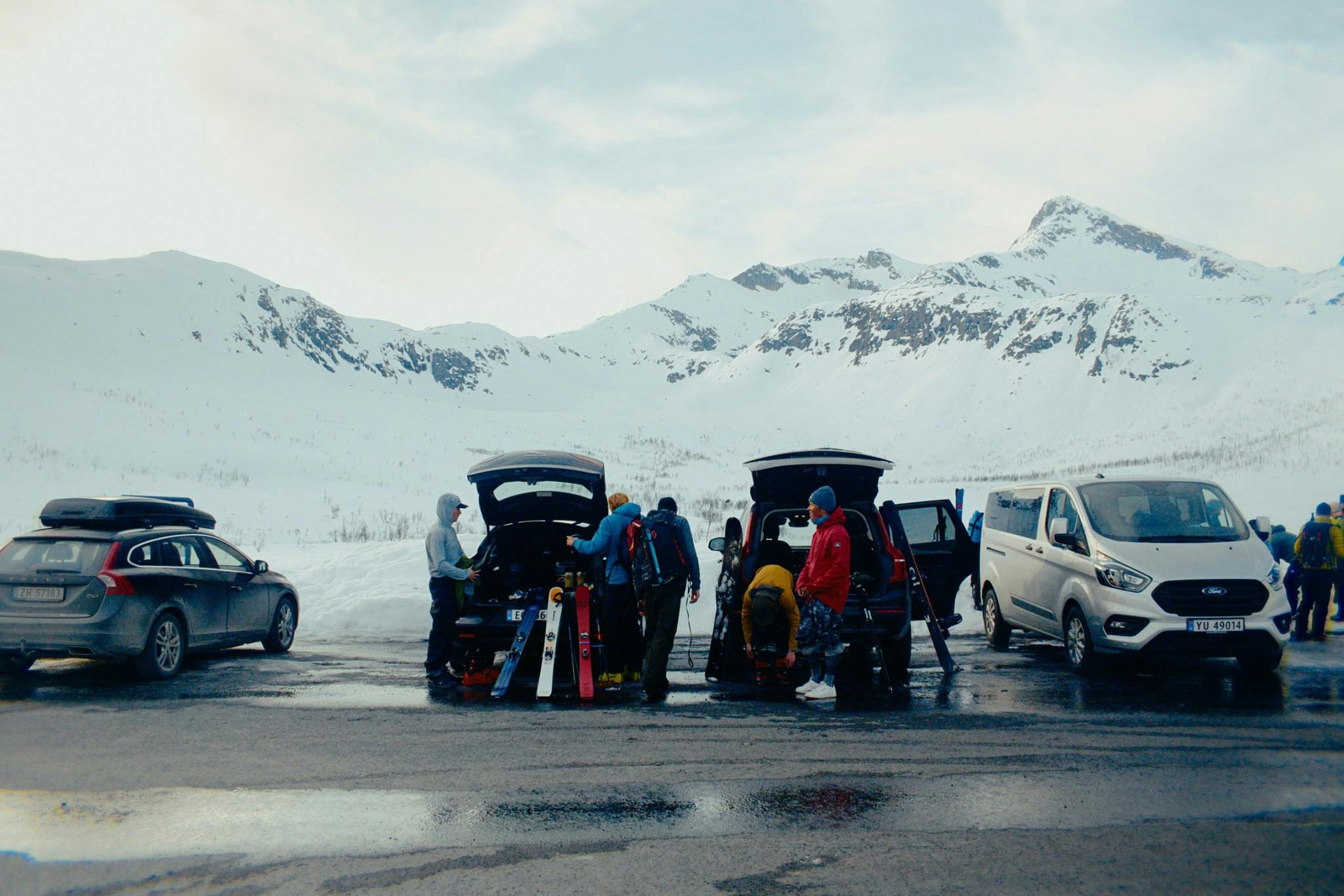 People surrounding two cars with a snowy peak in the background
