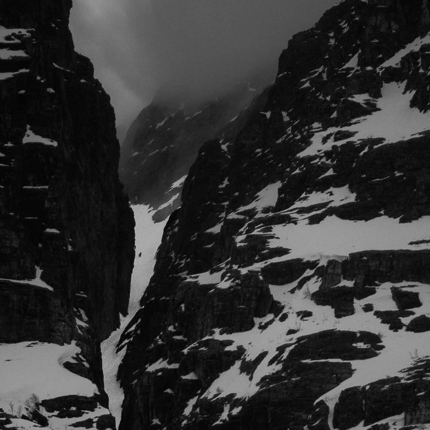 A black and white photo of skiers climbing a couloir between two mountains