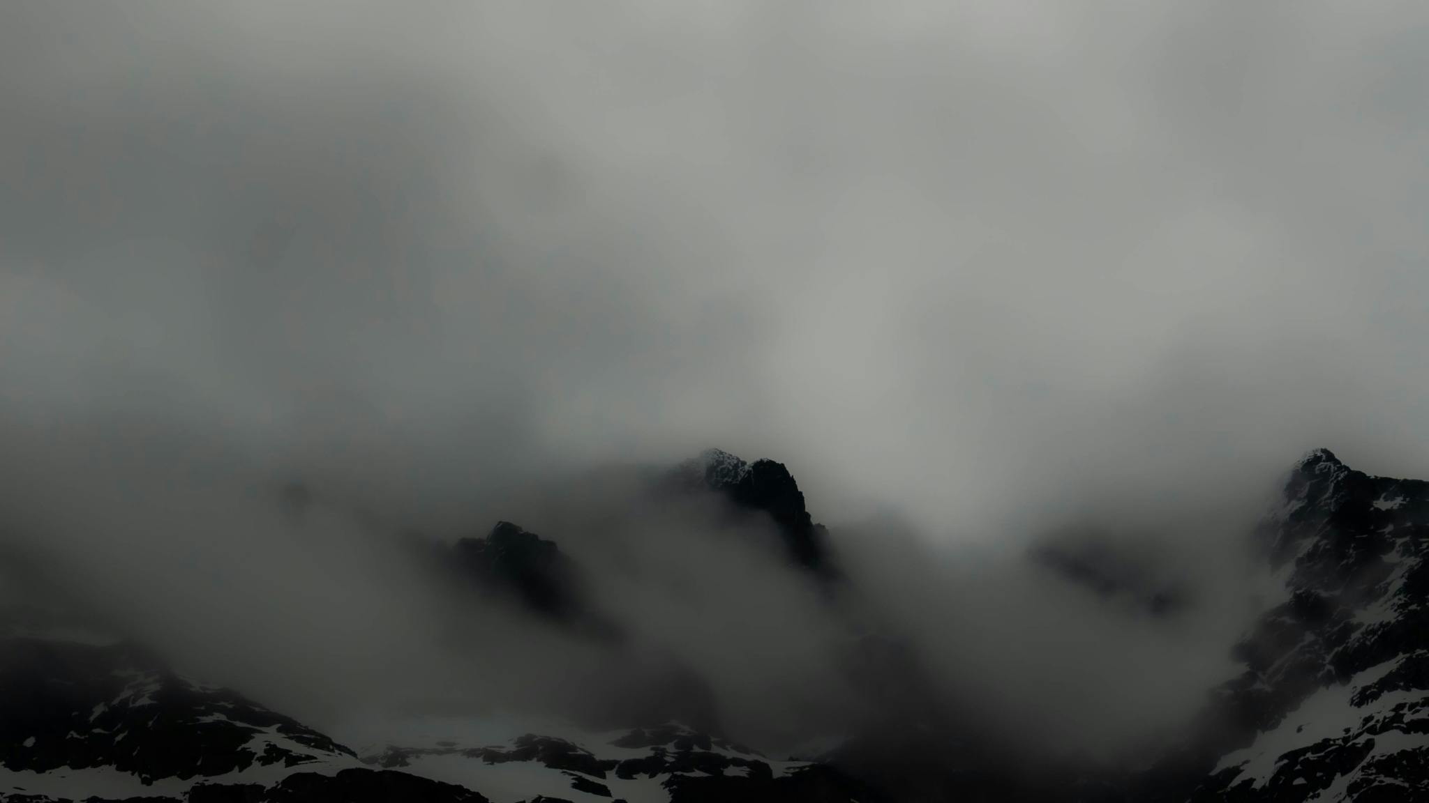 A black and white photo of mountains sticking out through clouds