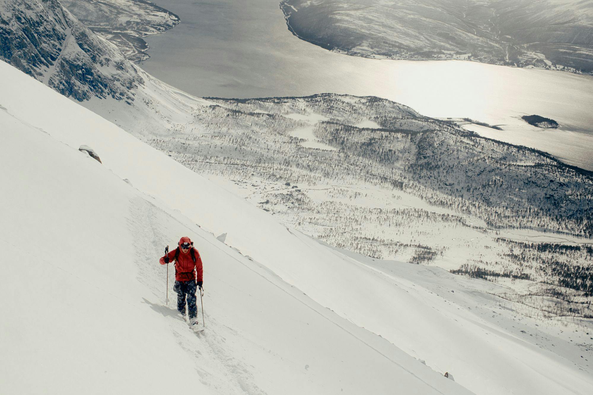 A skier climbing high up on a mountain with the arctic ocean in back