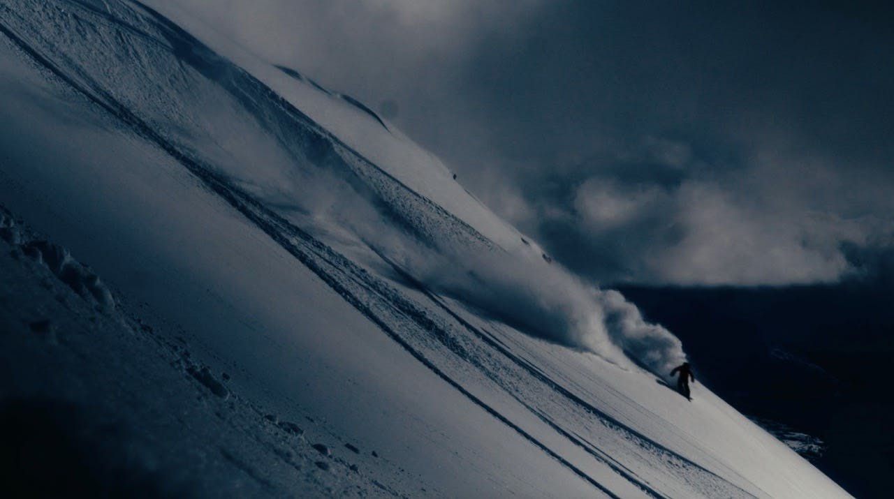 A snowboarder spraying powder in a dark environment