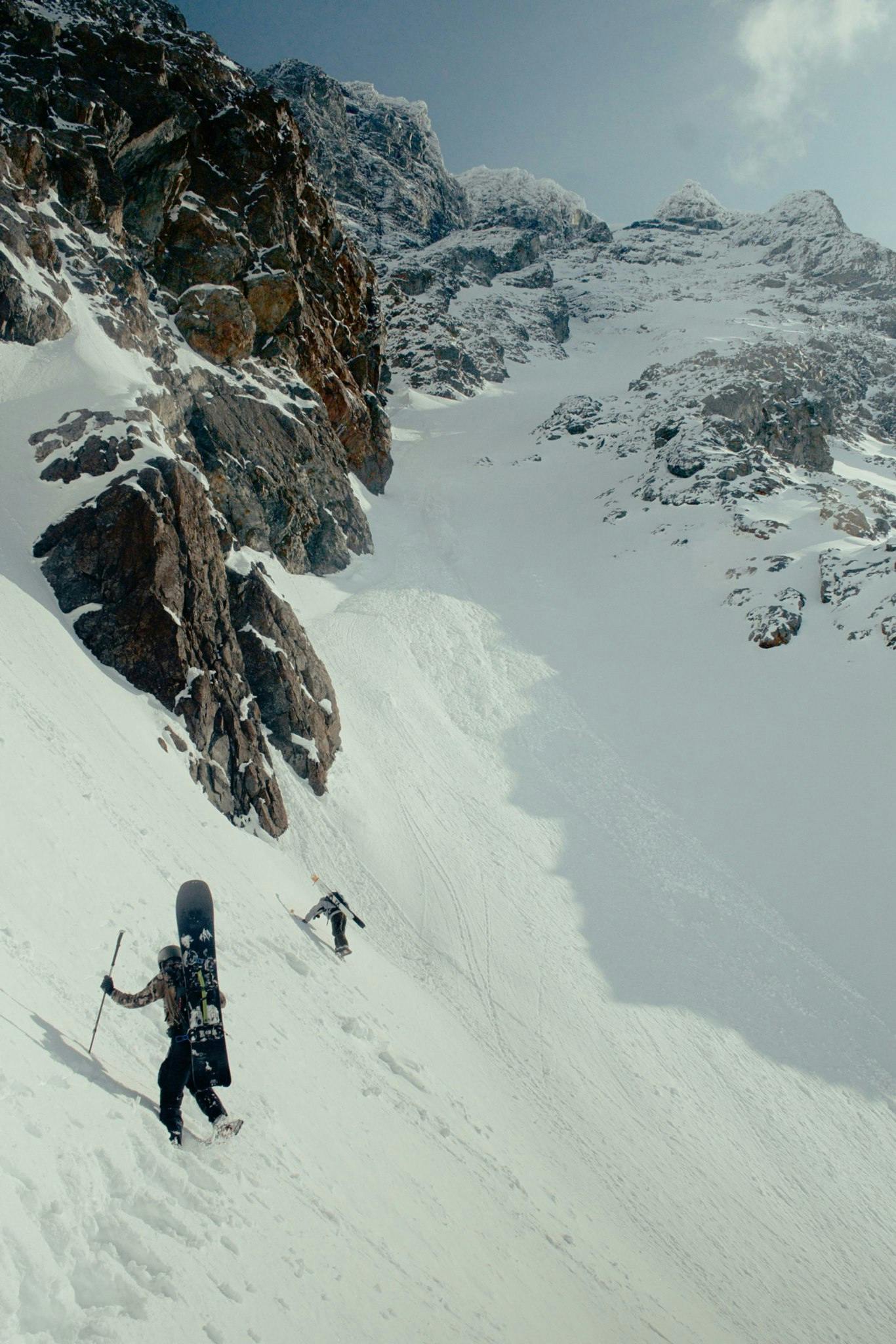 Two skiers climbing a mountain with skis on their backs