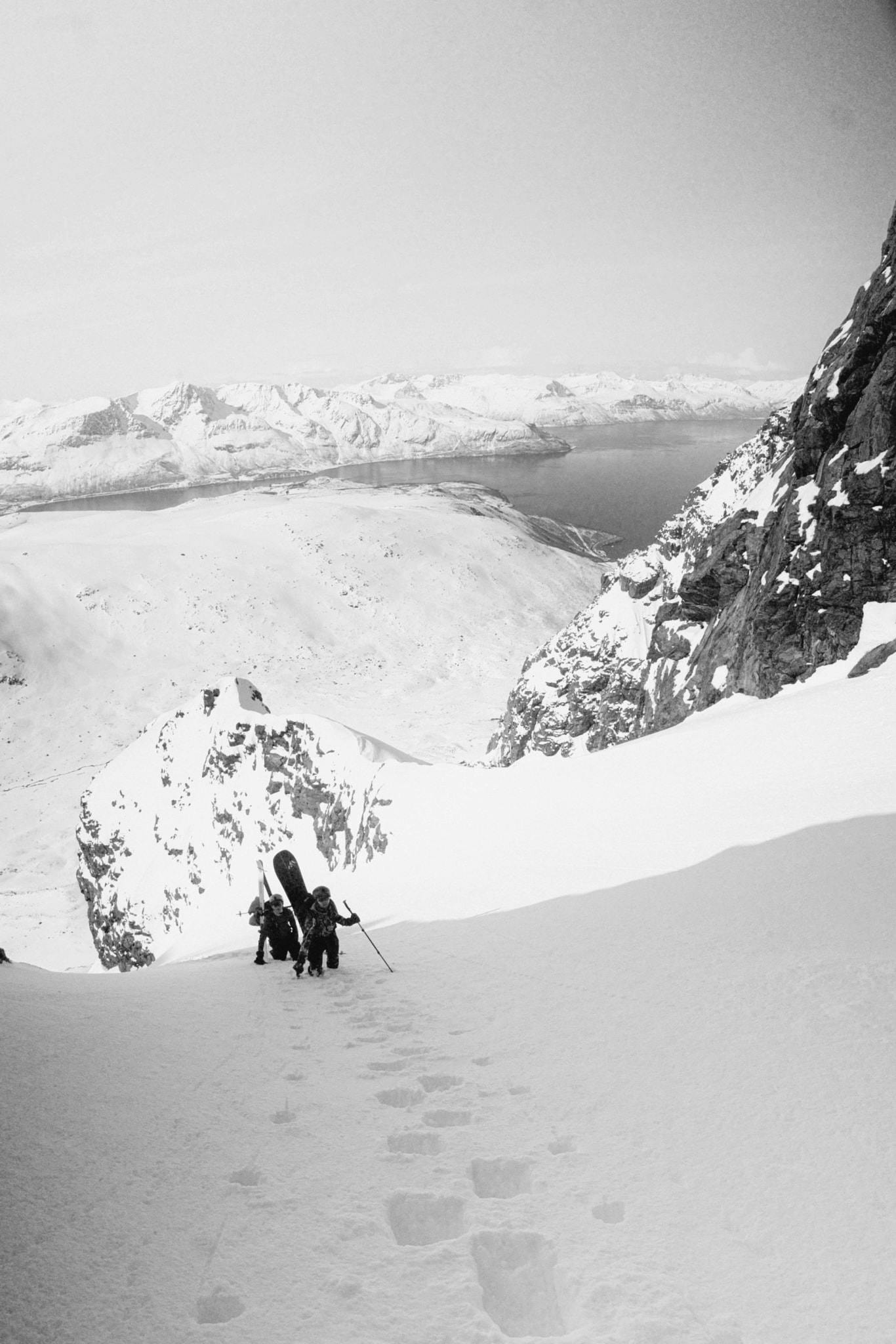 A photo down a snowy couloir with two climbers coming up