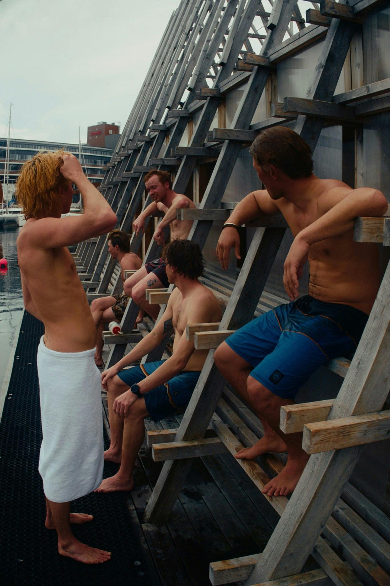 A group of men in swim trunks sitting on a dock