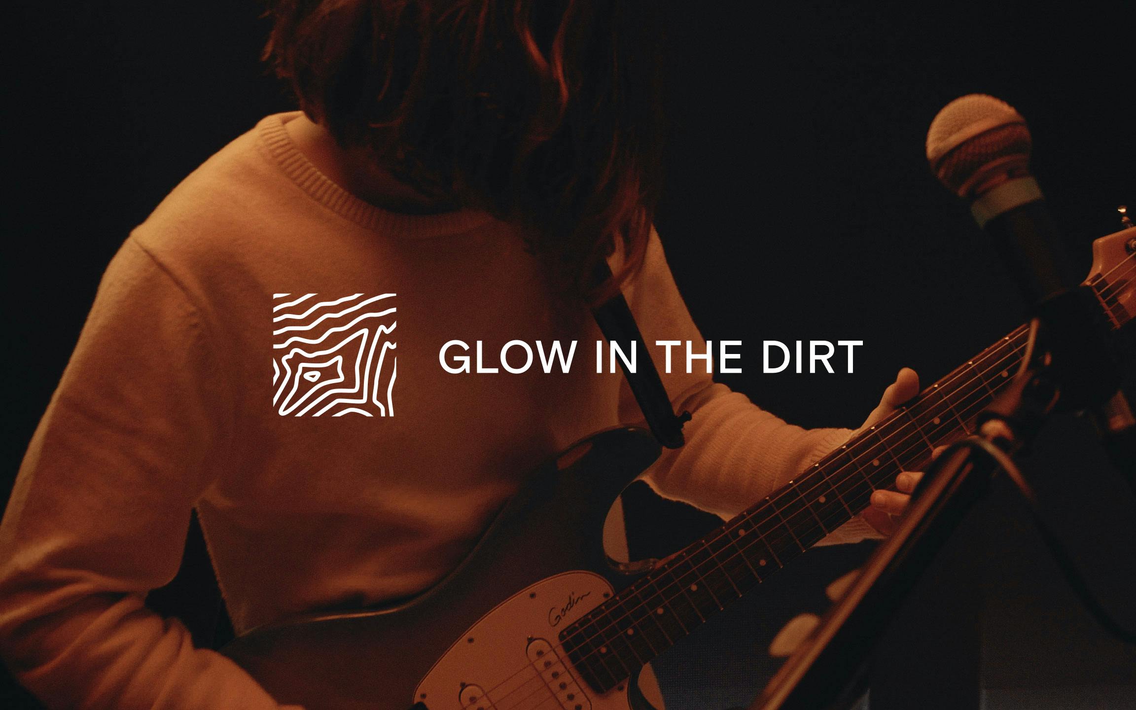 A photo of a man playing guitaer with the glow in the dirt logo on top