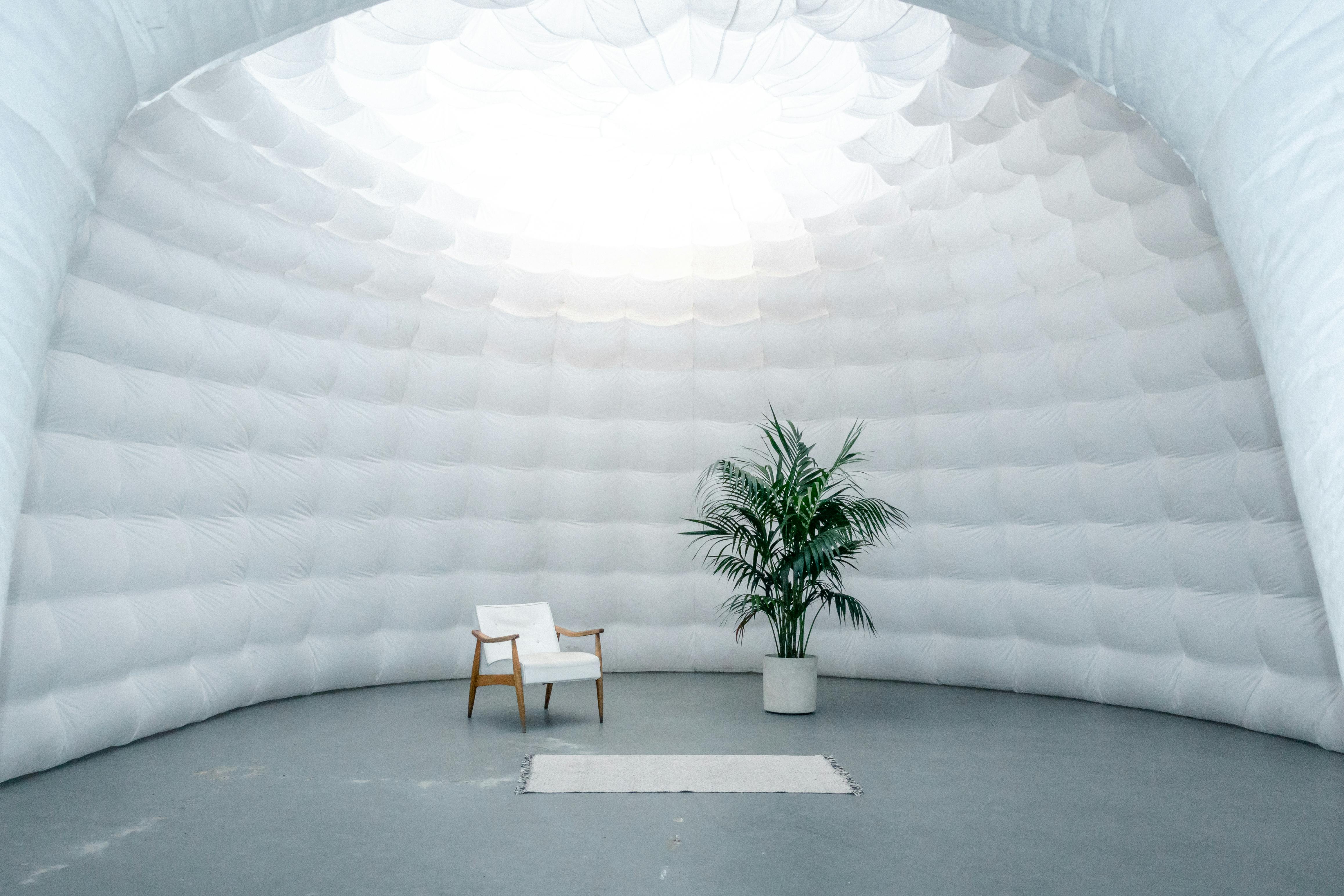 A white inflatable dome with a chair and tree inside