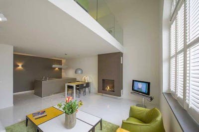 Kamer met keuken, open haard, televisie en groene stoelen 