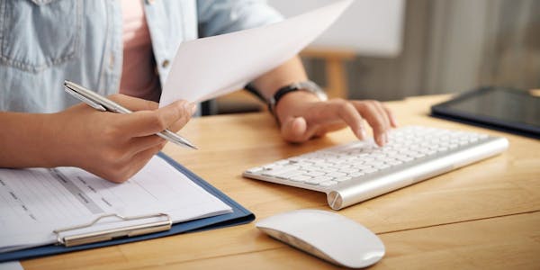 persoon die een papier vasthoudt en op een toetsenbord tikt